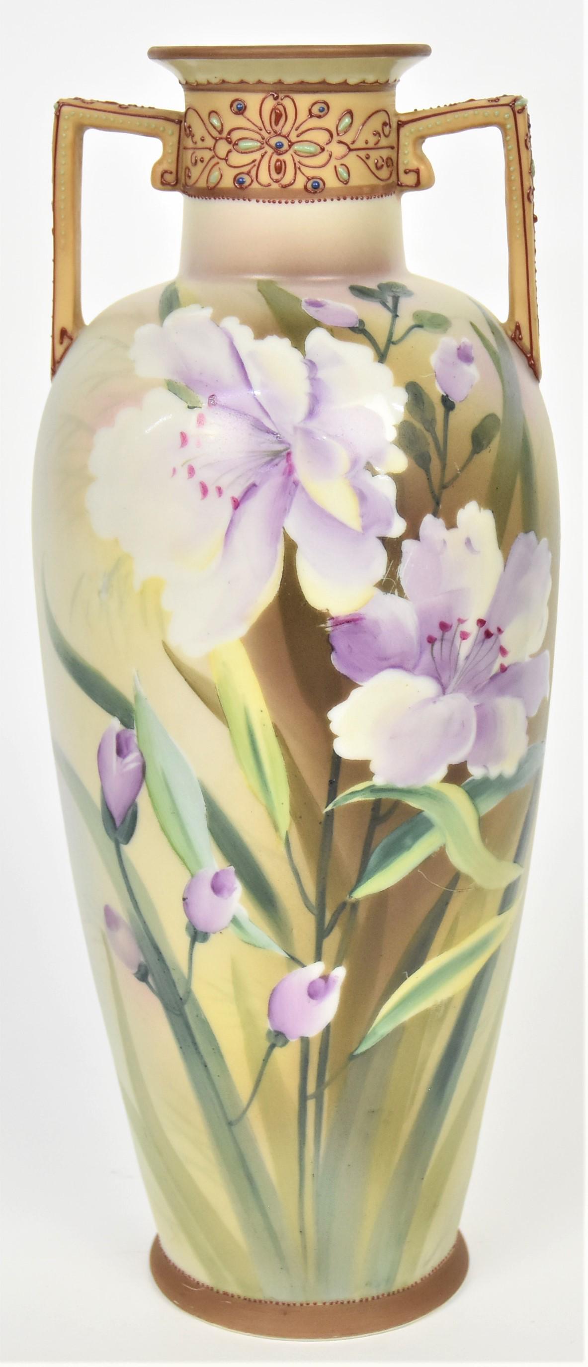 Nippon Jeweled and Floral Vase: The neck and handles have enamel jewels and scroll work. Lilac painted florals on the front, 11 1/4" tall. Maple leaf logo. Pleasant design, good condition.