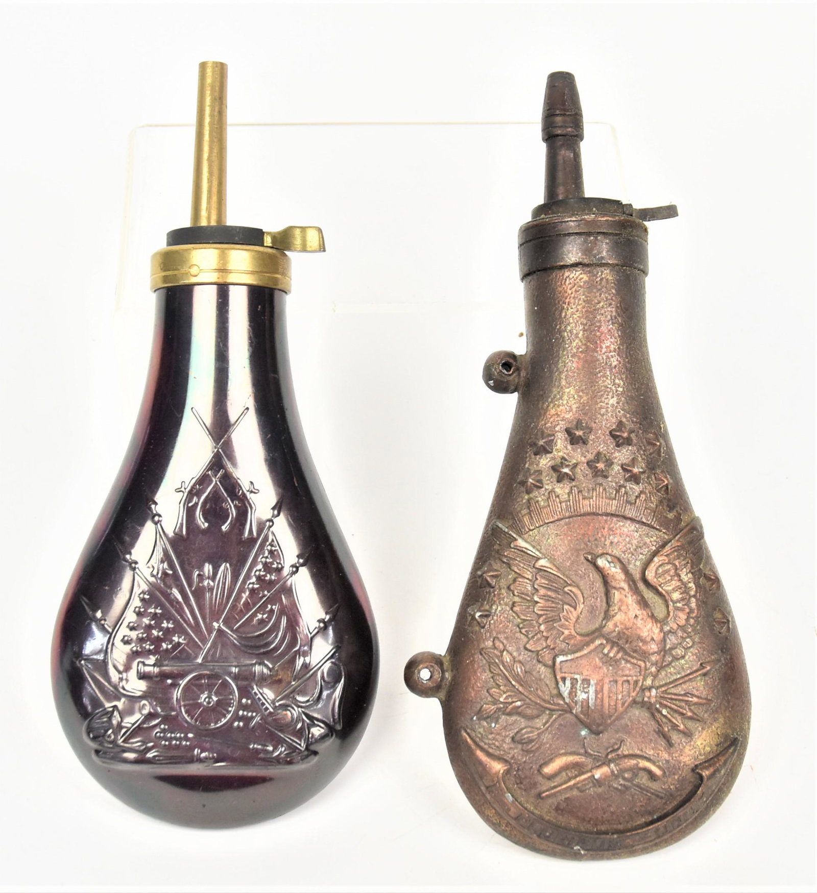 Two Military Powder Flasks: Including a brass example with cannon with crossed U.S. flags and arms on each face, 8" high; and bronzed cast white metal with U.S. shield breasted spread winged eagle clutching arrows and olive bran