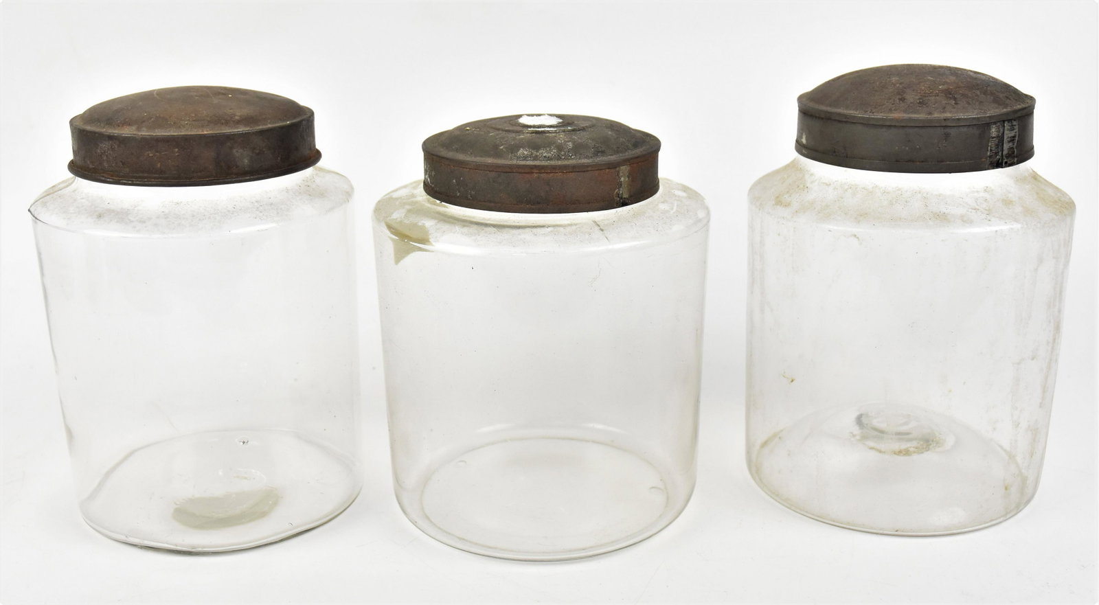 Three Blown Glass Pantry Storage Jars: All with original domed tin lids, largest with snap pontil, 5 1/2" diameter x 8" high; 5 1/2" diameter x 7 3/4" high; & 6" diameter x 7" high. Condition two smaller with minor nicks at lip, covered by