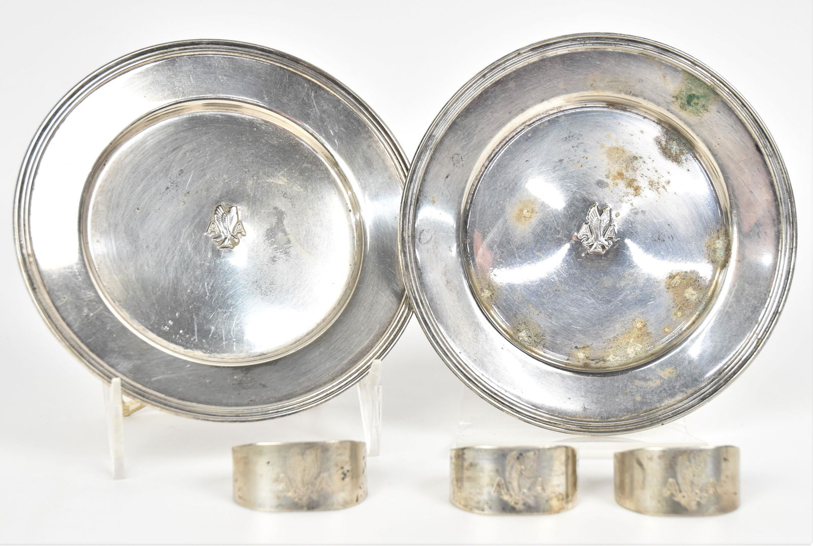 American Airlines Silver: Lot of five, all silver plate, incliding three matching napkin rings with eagle I flight and AA engraving, 1 3/4" long; and two matching 6" plates/saucers with stamped eagle in flight flanked by AA, a