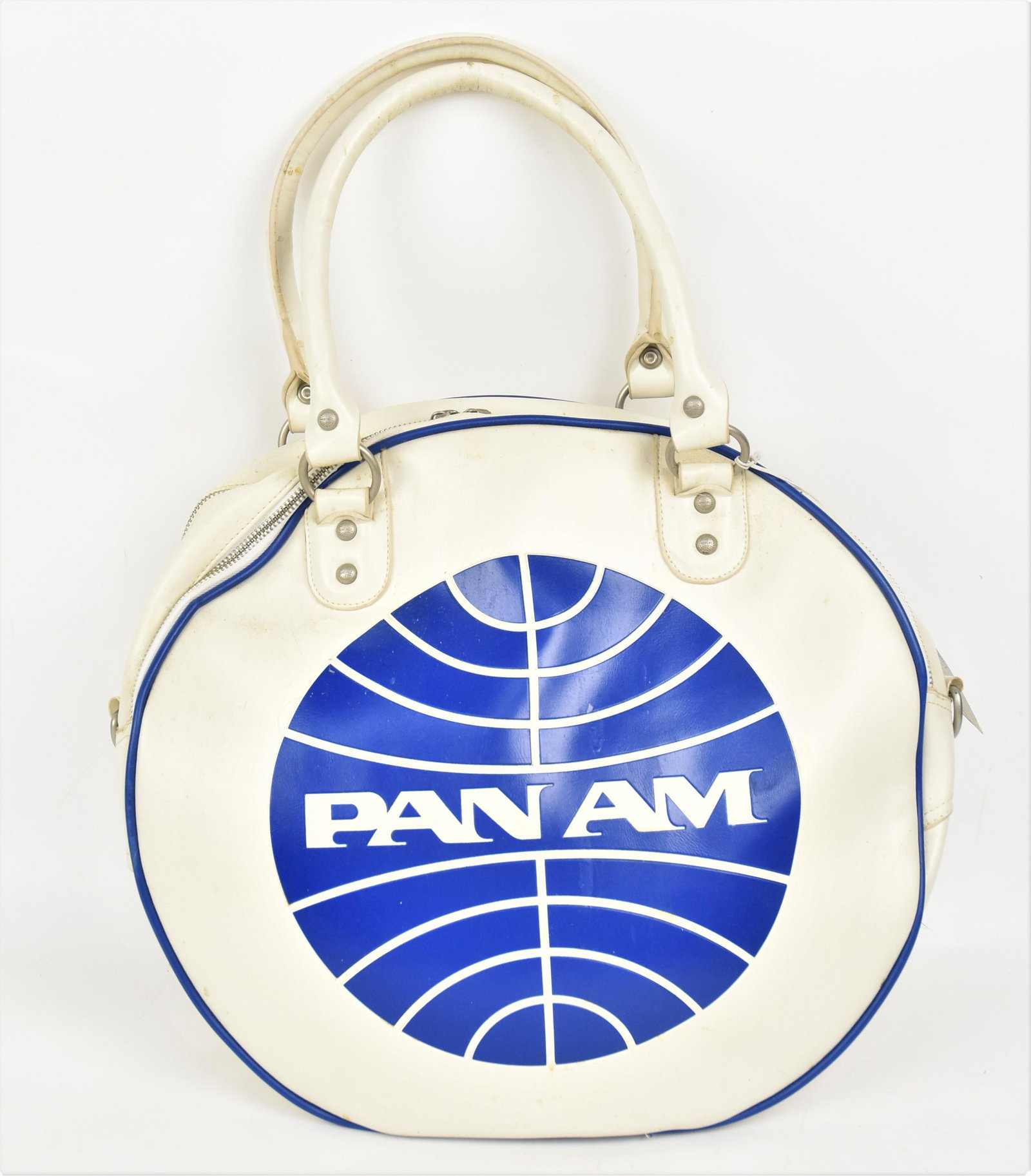 Pan Am Carry On Bag: White leather circular form with flat base embossed with company logo on each face with two leather swing handles. Two double handles zipper closures with cast metal handles in form of compny logo, an