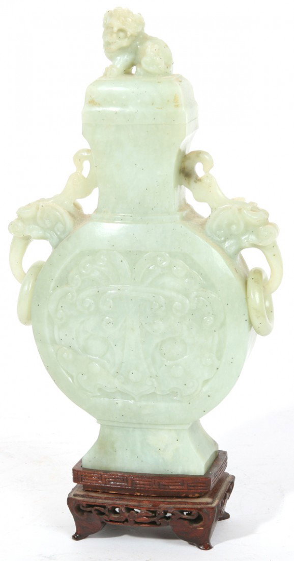 CHINESE CARVED GREEN JADE VASE ON STAND: Flat sided with stylized relief floral panels, elephant head handles with hanging rings, lid with foo-lion finial on carved teak stand. Very fine condition. 10" high.