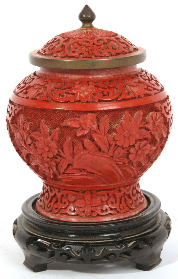 FINELY CARVED CHINESE CINNABAR COVERED JAR: With intricately carved geometric ground and floral landscapes, on brass body that was enameled on interior before application of cinnabar, on carved ebonized base. Excellent condition. 7.25"