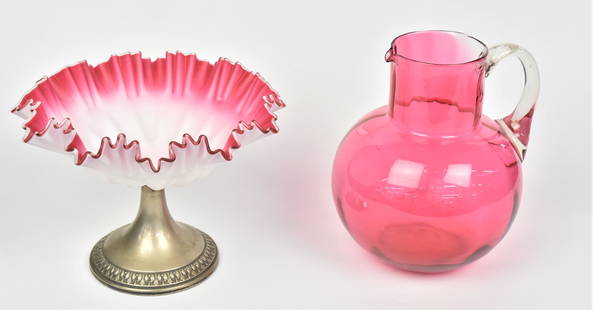 Peachblow & Cranberry Art Glass Pieces: Lot of two including a satin peachblow compote on unmarked silverplate base 6 1/2" x 9"W; and a ribbed cranberry water pitcher with clear handle 8". Condition VG.