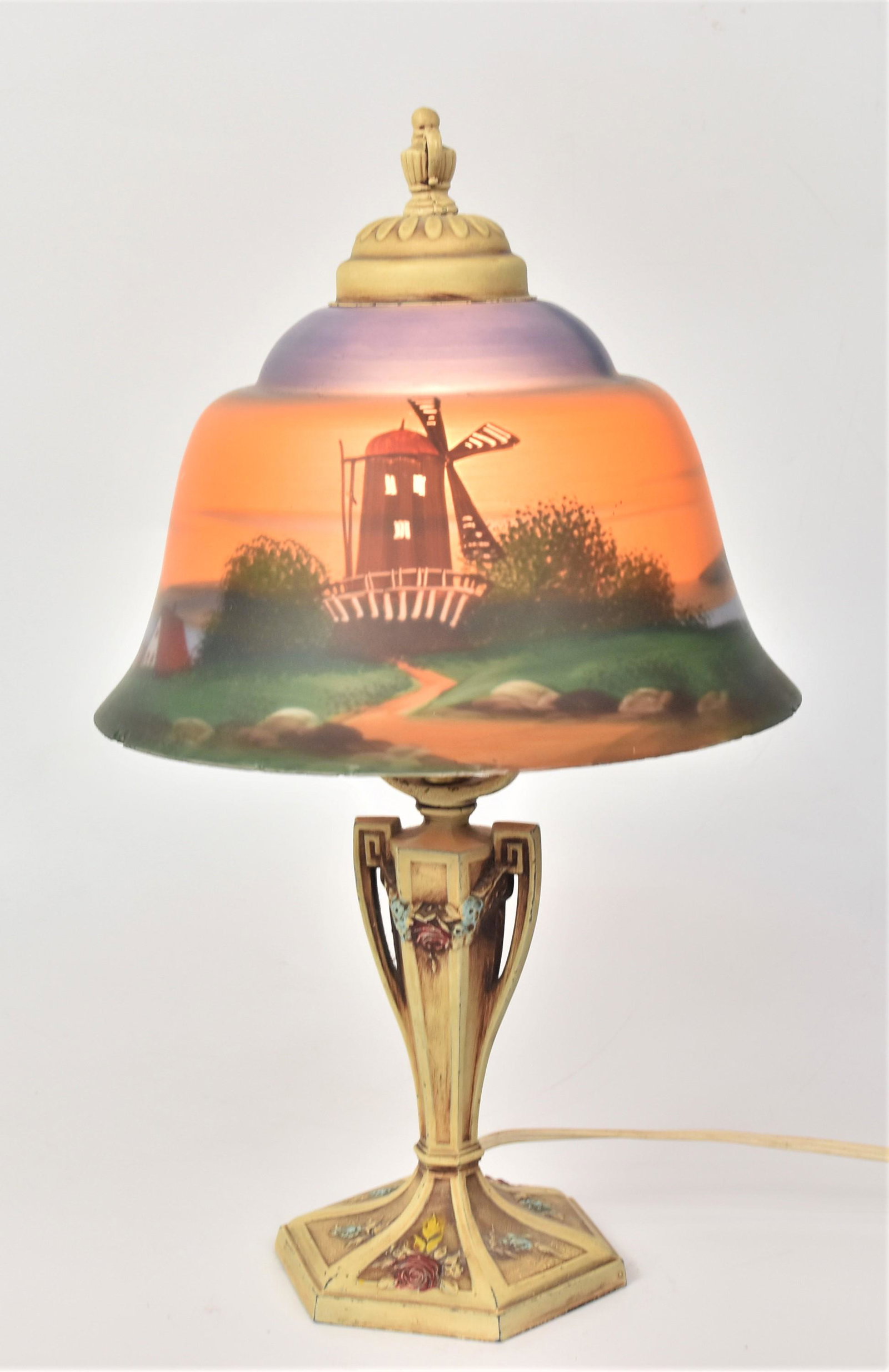 Reverse Painted Boudoir Lamp: 9" diameter bell shaped polychrome painted glass shade with Dutch landscape with windmill, mounted on original polyhrome paint iron base with relief cast rose swags, 15" high. Condition small flakes a
