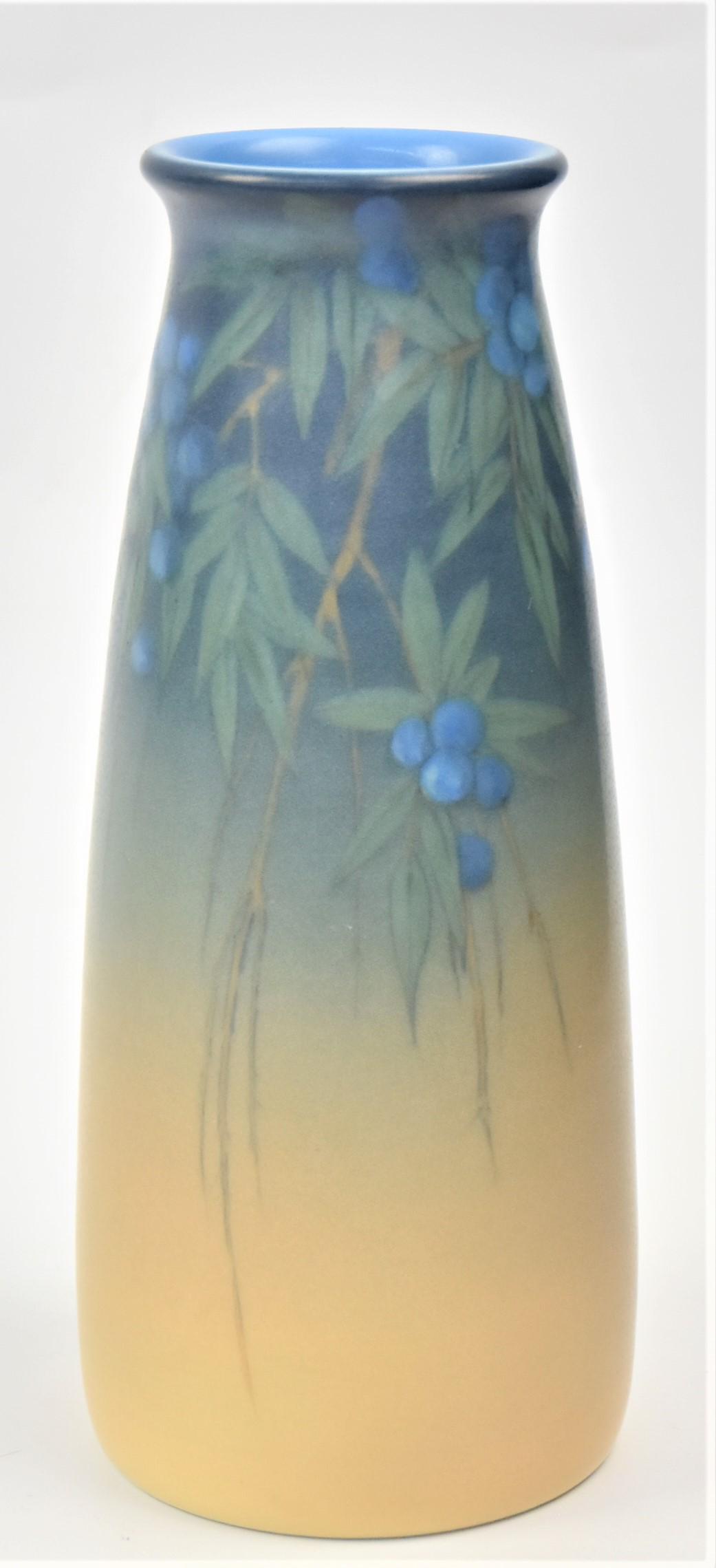 Nice Rookwood Vellum Vase: By Lenore Asbury. Date 1927. Shape 1660E. Gathers of blue berries among spiked foliage dangle the rim. Measures 7 1/2"H. Incised artist monogram and the incised V for vellum glaze. Impressive vessel. 