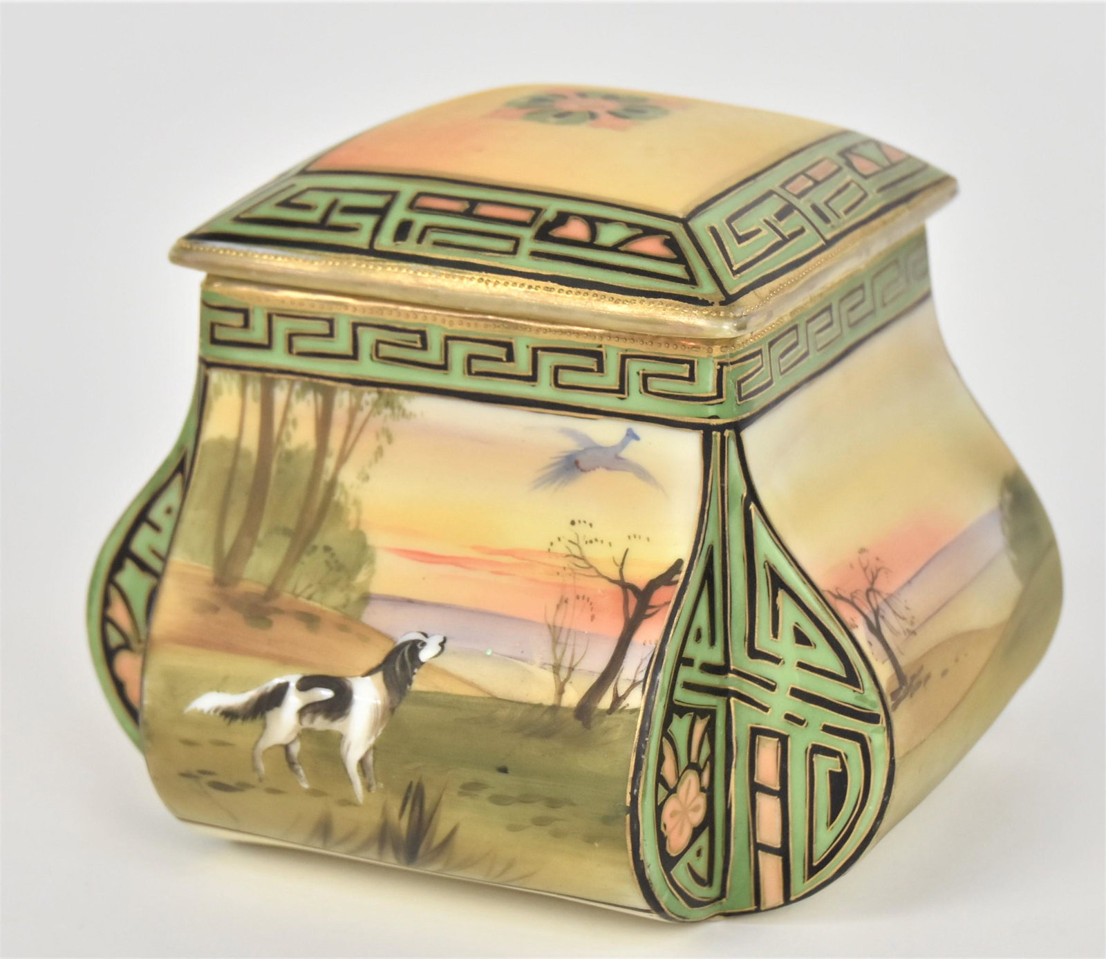 Nippon Covered Humidor: With a springer spaniel having flushed a pheasant & landscapes all around. Greek Key design. 5”T. 6 1/4”W. Four faint lines inside cover. Repair to containers corner. Unusual form. Handsom