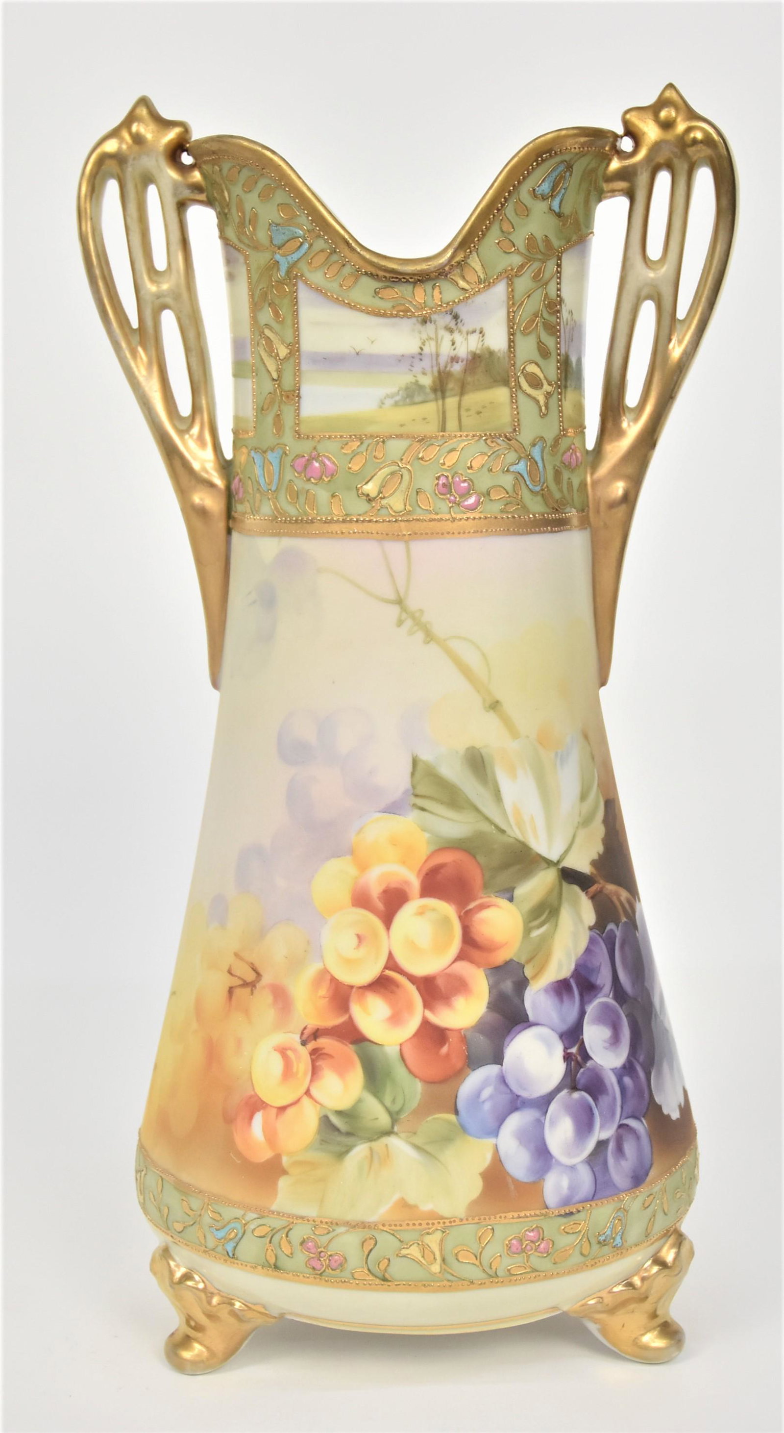 Large 13.5" Nippon Jeweled & Enameled Vase: With life-size grapes. Pleasing landscape views are on the collar. Fancy pierced gold handles With mild handling wear. Gold scroll feet. 13 1/2”T. 6 1/4”W. Good condition. Green mark.