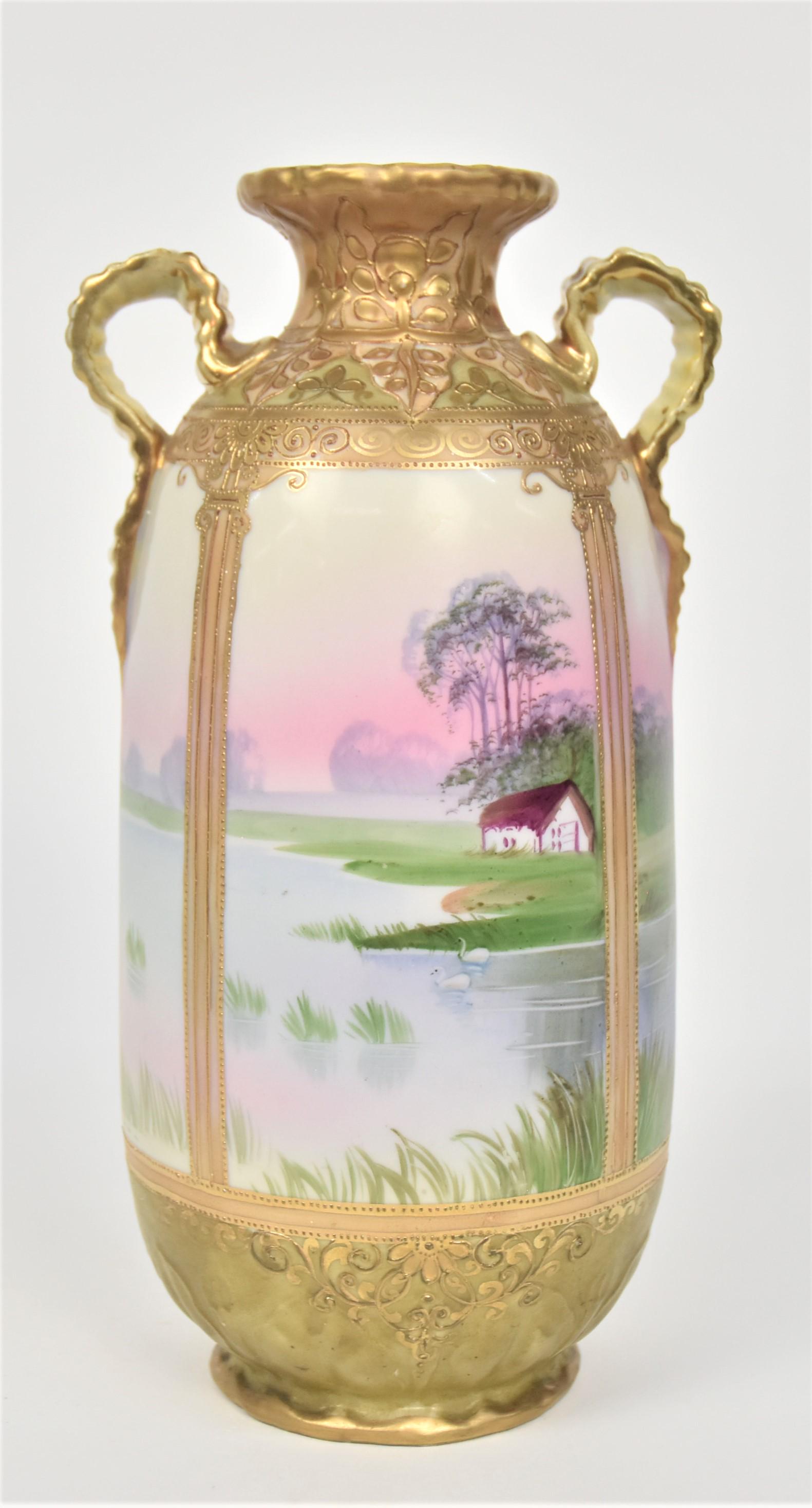 Nippon Tall Vase With Golden Pergola Columns: With raised gold designs provides a view of a serene lake With swans and a shore side cottage. Gold enhanced fancy crimped handles. Lower body has leaves & Cala lilies in relief. 11”T. 5”D