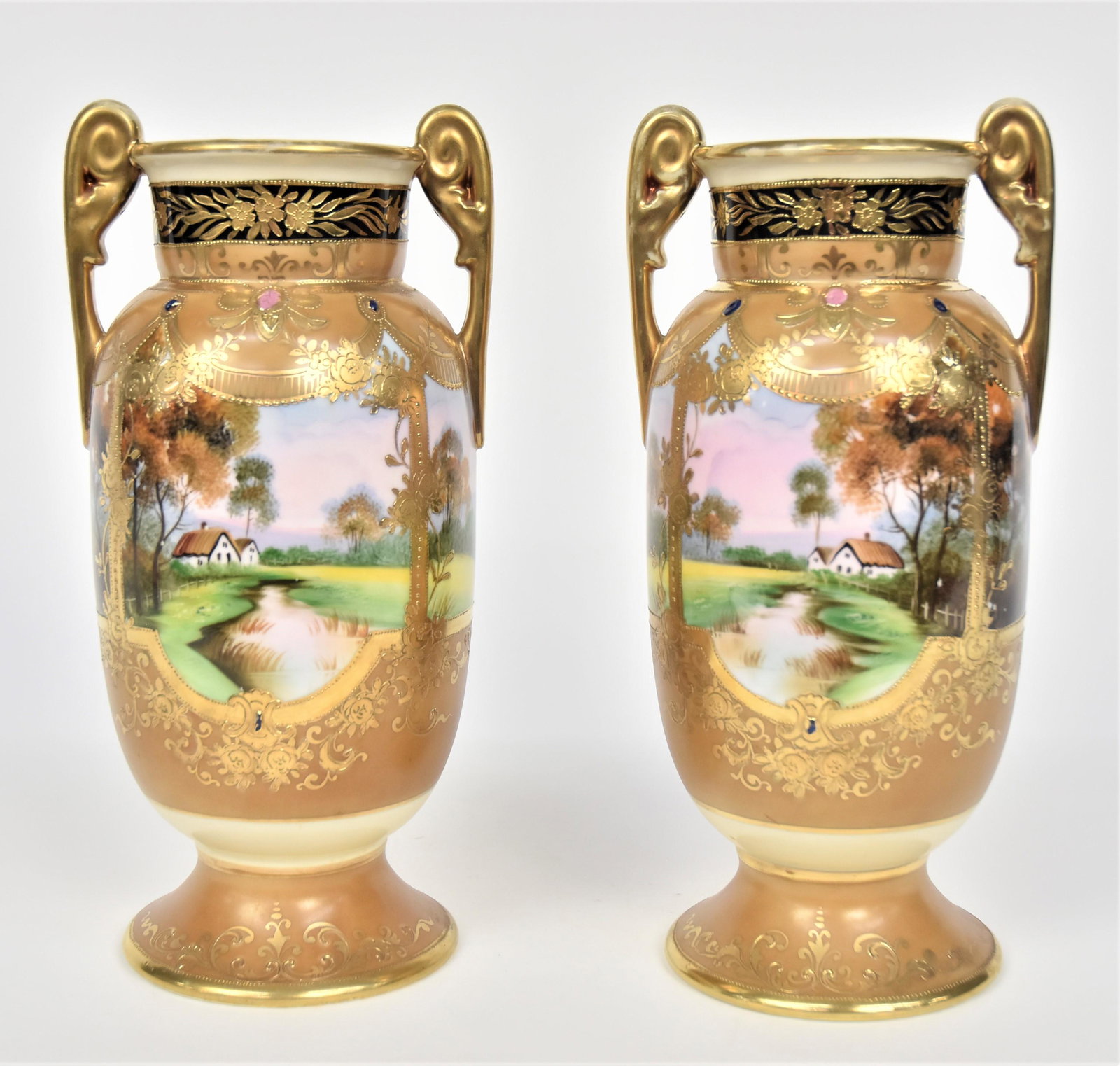 Pair Nippon Mirror Image Gold & Jeweled Vases: With scrolled handles. Colorful summertime landscape With cottages lakeside. Both are 10 1/2”T. 4 1/8” bases. Handsome pair in very good condition. Blue marks to each.