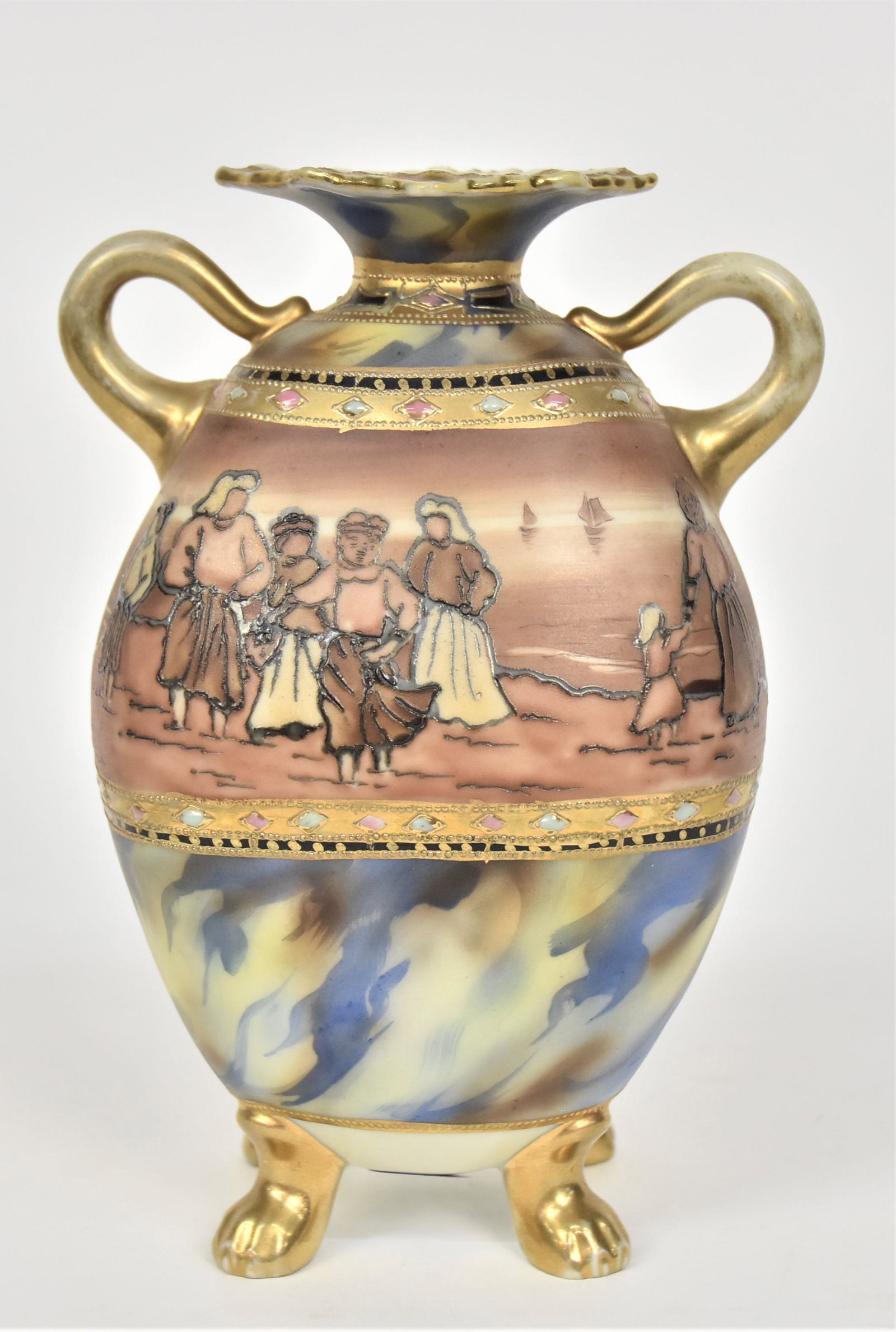 Nippon Jeweled & Gold Vase: Featuring a gathering of women waiting at the shore for the arrival of the ships on the horizon. Flame-like decoration on the rim & base. Gold loop handles & four mammal feet. 7”T. 5”W Wit