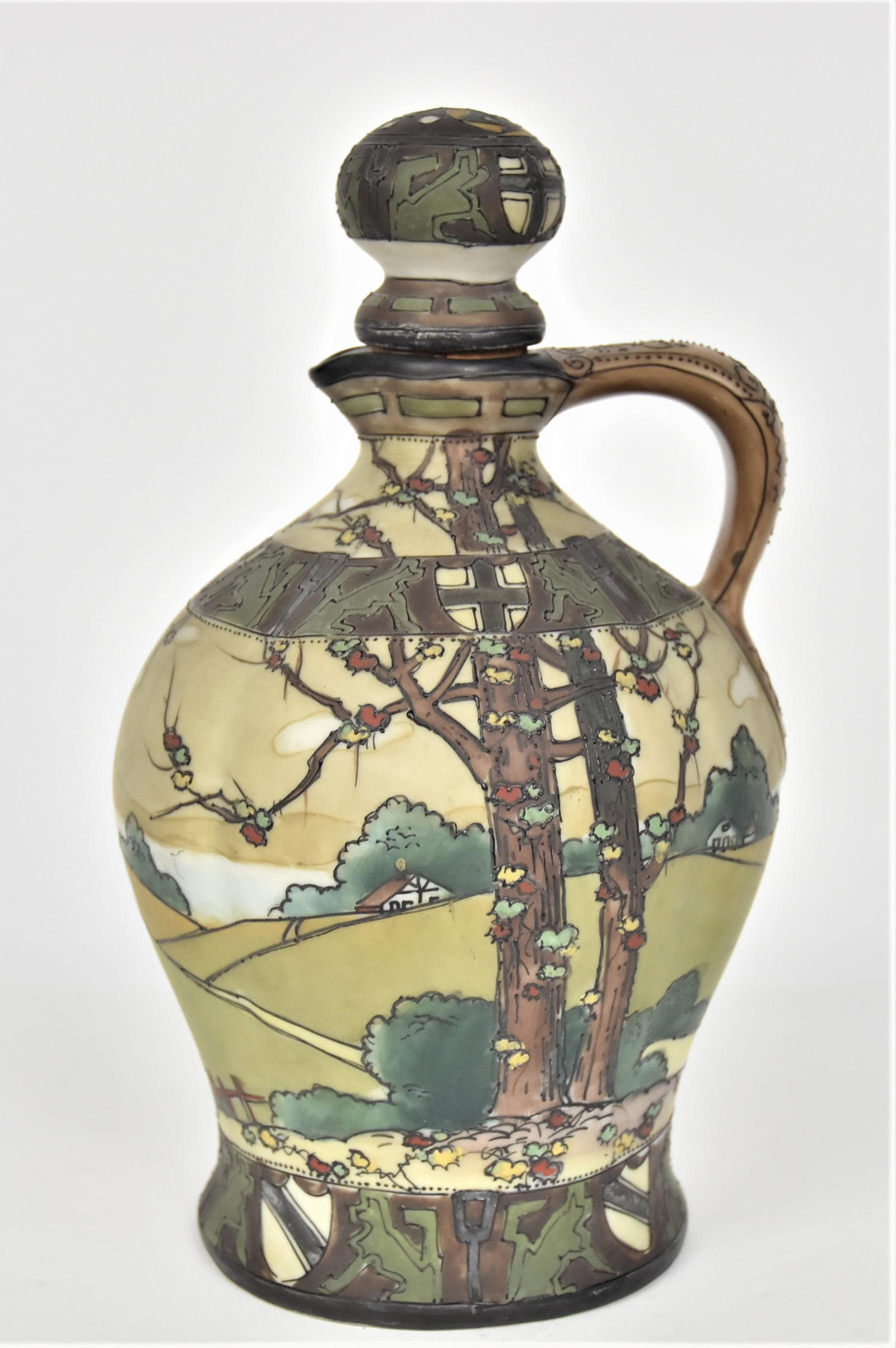 Nippon Whiskey Jug Dark Woodland: With matching stopper. Peering through autumnal foliaged trees onto a hilly country landscape With houses. Decorative bands of Griffins & shields. Enameled handle. 9 1/4”T. 5”D. Handsome j
