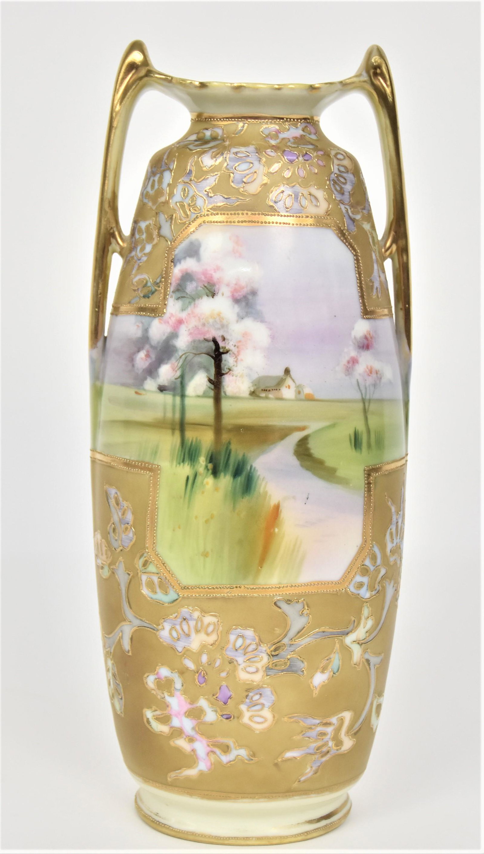 Nippon Spring Scenic Handled Vase: Bordered by pastel flowering branches, enhanced by raised gold outlines. 12 1/2”T. 4 3/4”W. Very good condition. Green mark.