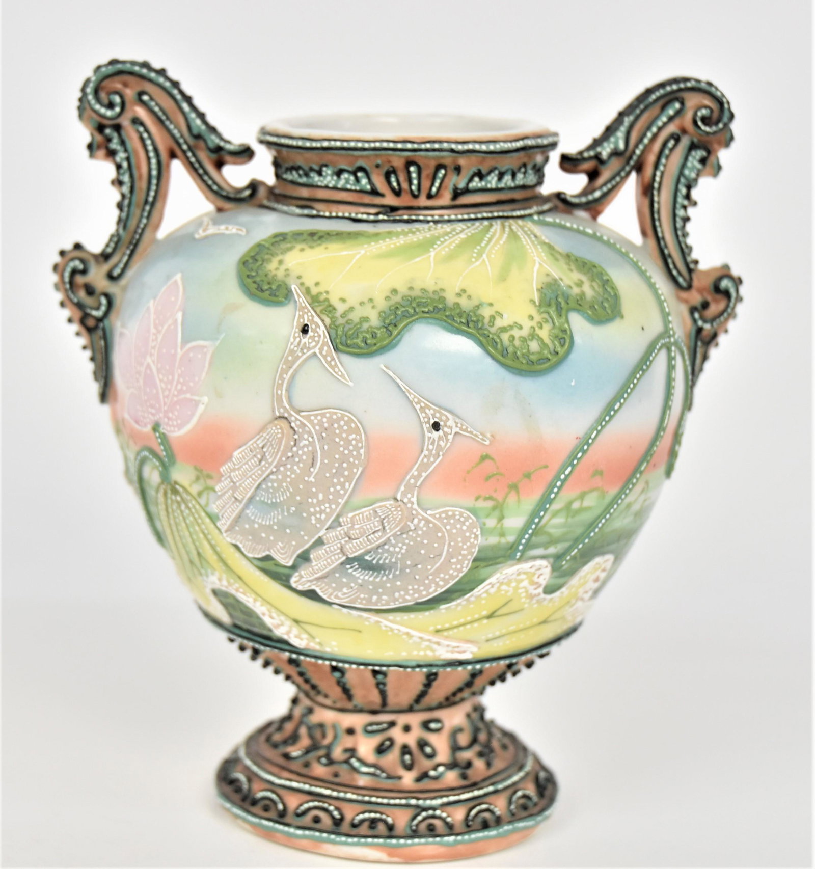 Nippon Moriage Vase With Egrets: Pond lilies, foliage & birds in flight. Fancy embellished dolphin handles. Highly decorative base. 6 1â€™2”T. 5 3/8” across handles. Showy & in very good condition. Green mark.