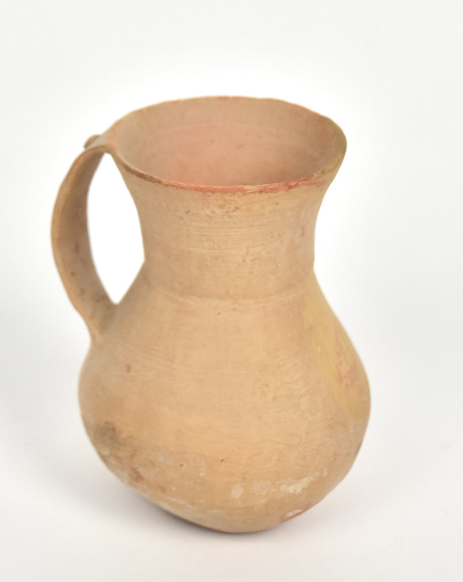 Greek Pottery Pitcher 8 th Century B.C.: Wheel thrown tan terracotta with flared lip, thin strap handle attached at lip and shoulder with applied disc near top, Attic period, 3” diameter x 4 ¾” high. Condition Fine.