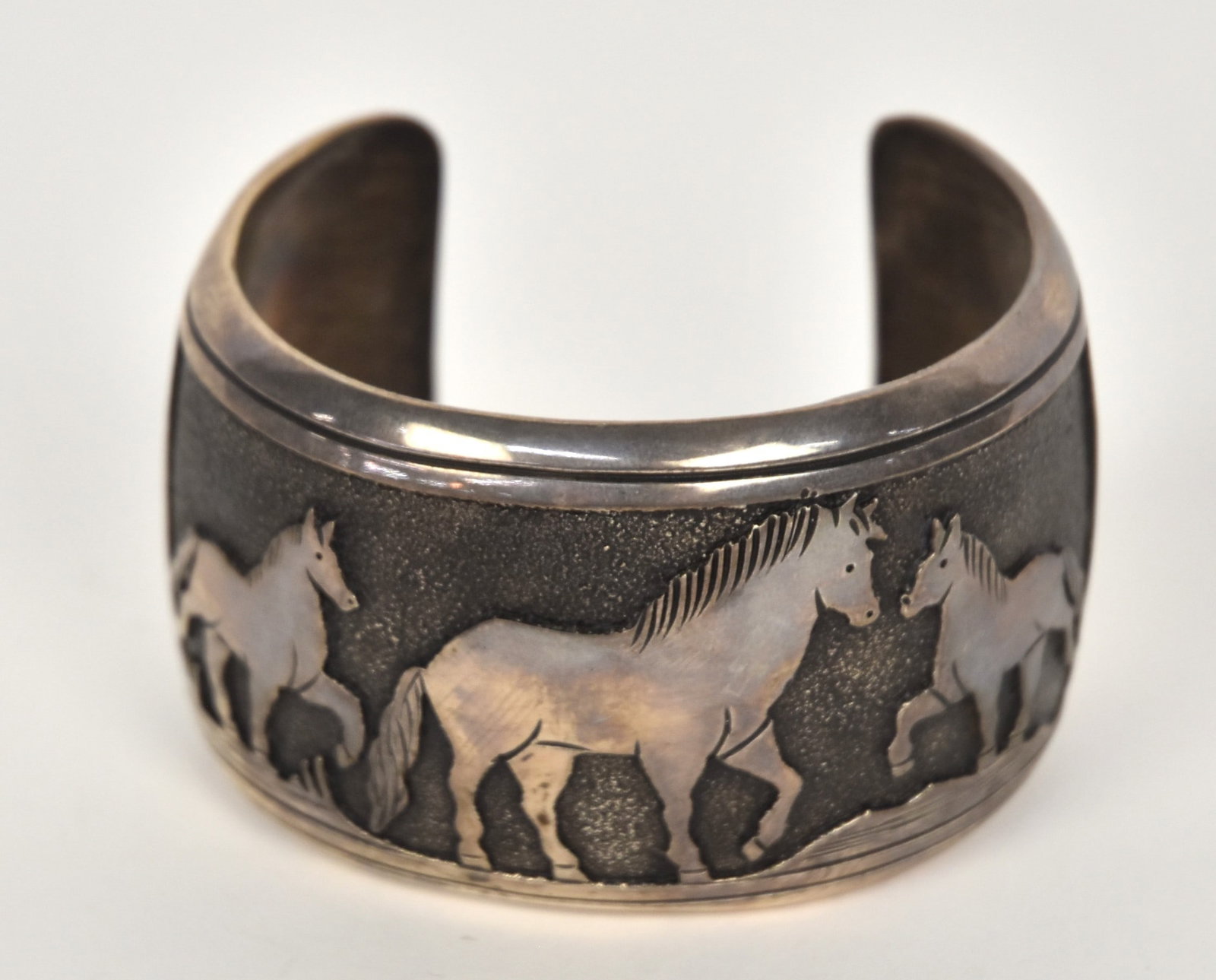 Thomas Singer Navajo Cuff Bracelet: Artist signed Thomas Singer, (Thomas Singer 1940-2014, noted Navajo silversmith) Sterling with three high relief horses and road runner tail feathers on stippled ground, 2 x 3 x 2 3/8", weight ?? Cond