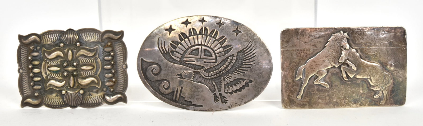Three Navajo Sterling Belt Buckles: Including one marked with D and an arrow and Sterling (Darryl Becenti, Navajo) with chased and engraved geometric motifs, 3 x 2 1/4"; plus rectangular with relief fighting horses, marked Sterling, 3 1