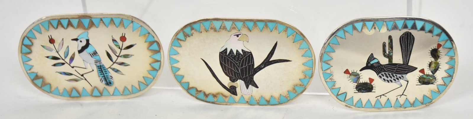 Three D&N Edaakie Zuni Sterling Belt Buckles: All oval and marked Dennis/Nancy Edaakie, including bald eagle perching, road runner with catis and perching blue jay, all with turquoise and other inlay, 2 1/2 x 1 3/4", total weight ??. Condition Fi
