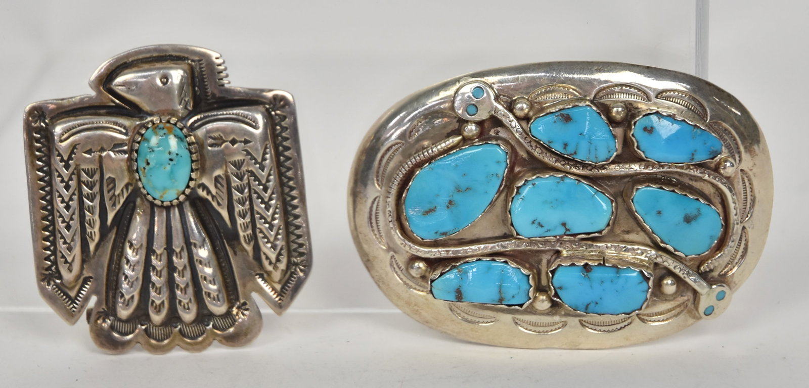Two Signed Navajo & Zuni Sterling Belt Buckles: Including one marked James Rogers in the form of chased fire bird with inset turquoise stones, 1 7/8 x 2 1/8"; and oval buckle with seven inset turquoise stones, and two rattle snakes with turquoise e