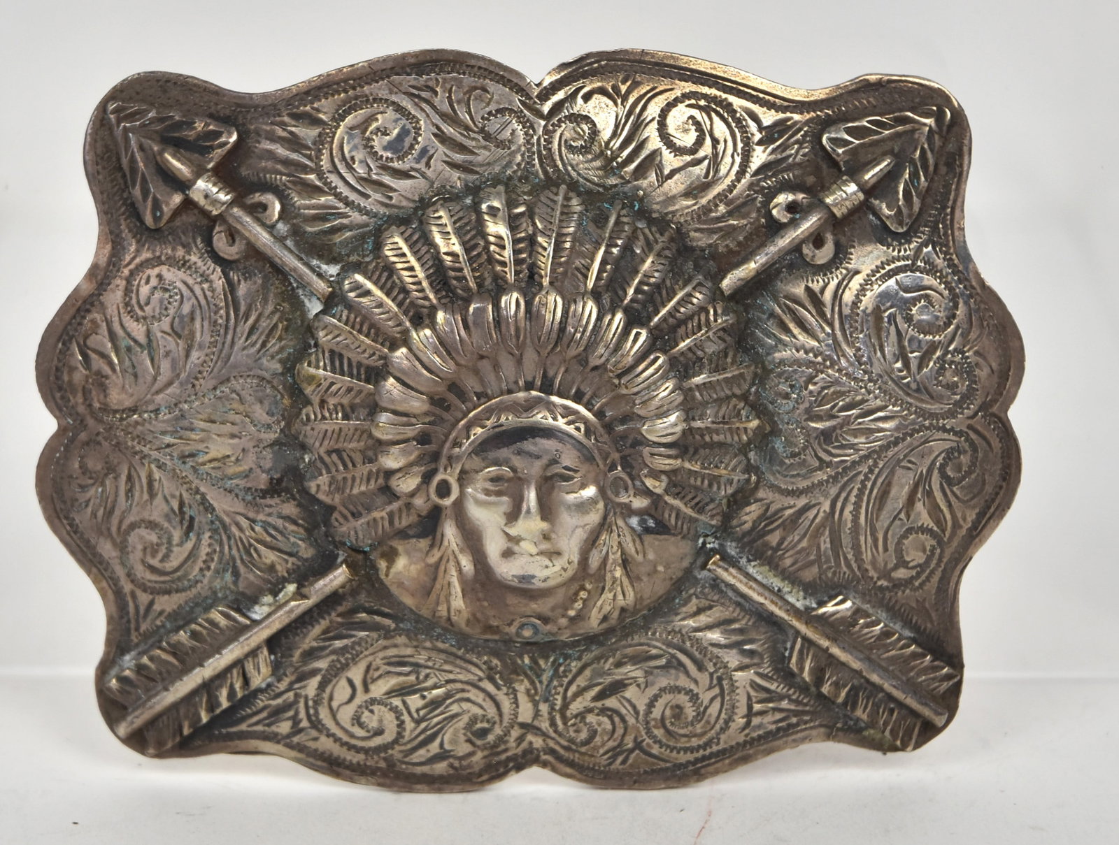 Marco D. Martin Sterling Belt Buckle: Houston Texas silversmith, signed on reverse with head of Plains Native American in full feather headdress with crossed arrows and engraved scroll work ground, 3 3/4 x 2 3/4", weight ??. Condition Fin