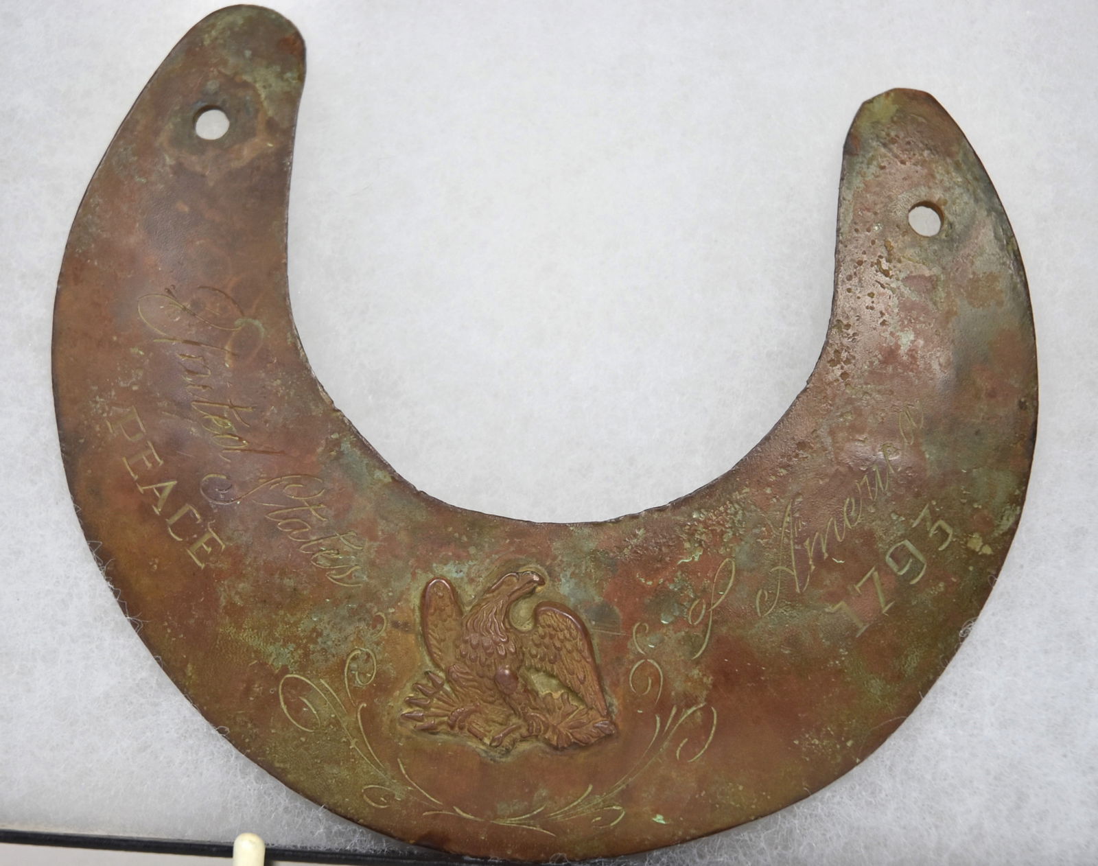 American 1793 Brass Peace Gorget: Dug patina with all over brown color, crescent form with two holes from suspension at ends, with Eagle clutching arrows and laurel branches in talons, engraved United States of America/Peace 1793 with