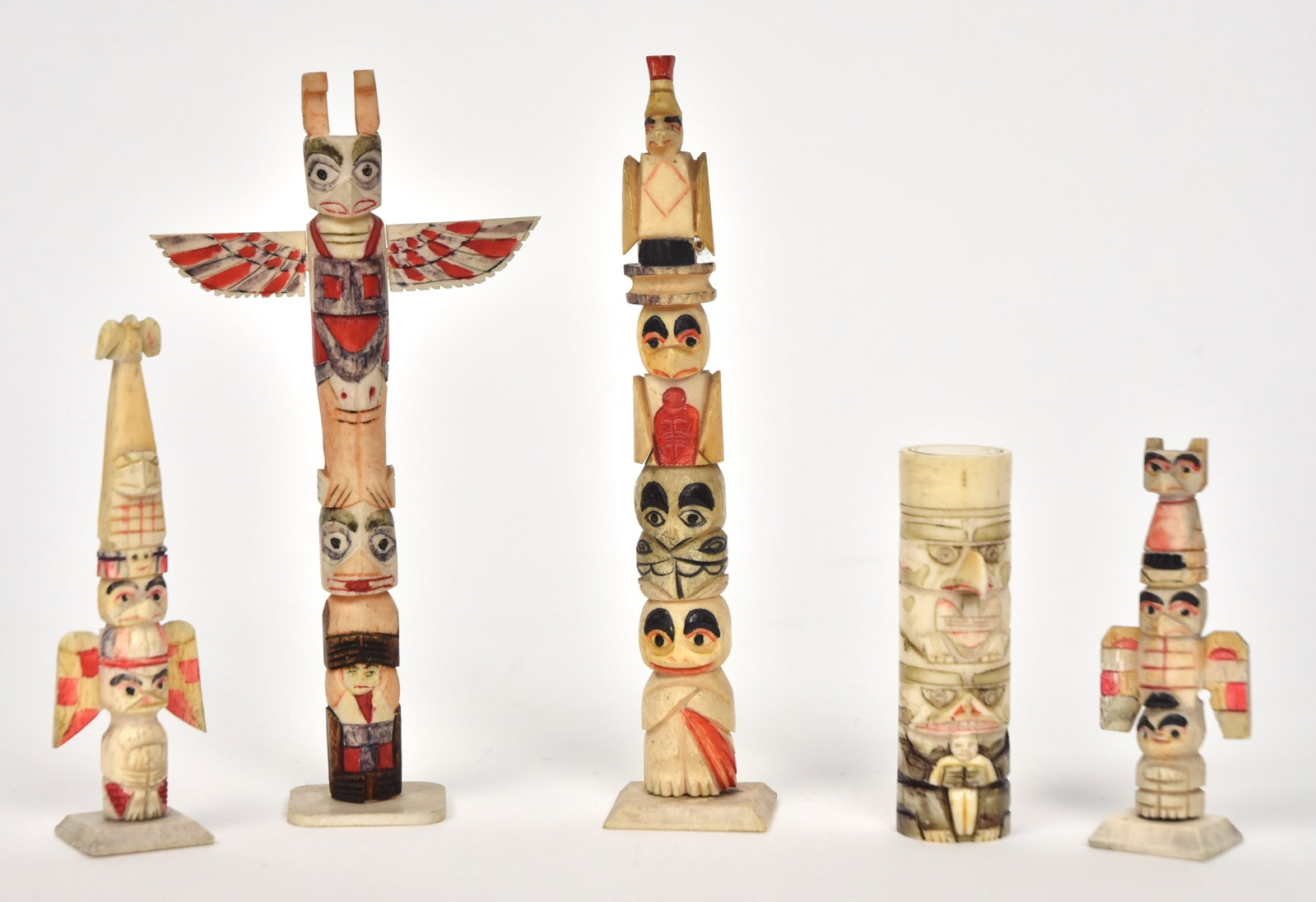 Northwest Totem Poles: Lot of five, all carved and painted bone, including largest with spread winged raven at top, 6 1/4", smallest is 4 3/8" high and last piece is a lidded dice cup in totem form with dice and threaded ca