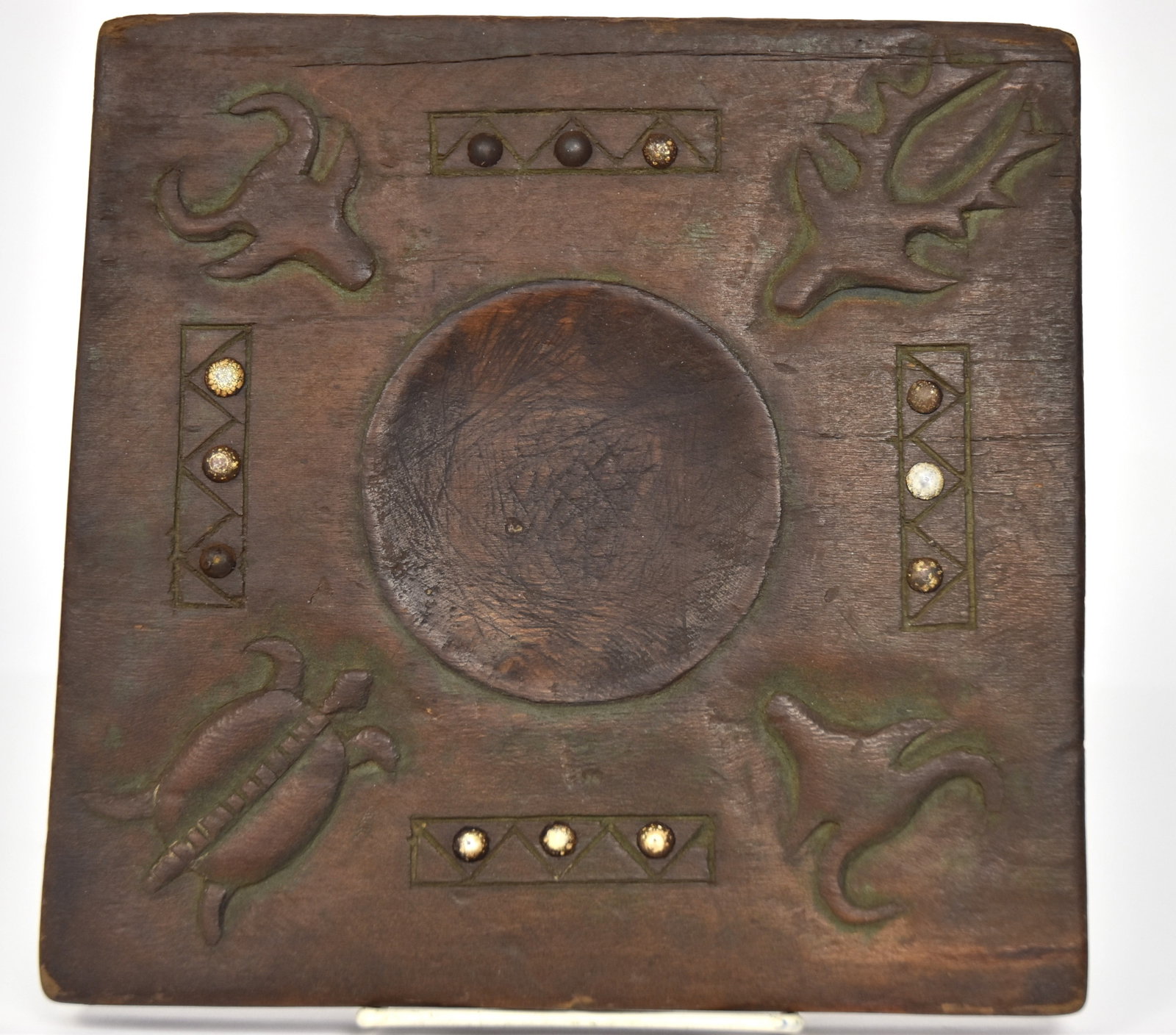 Reservation Period Sioux Tobacco Cutting Board: Circa 1890-1900 with nicely patinated pine or polar board with animal heads carved in the corners in low relief and turtle in fourth with four bars with chevrons and three domed tacks between, recesse