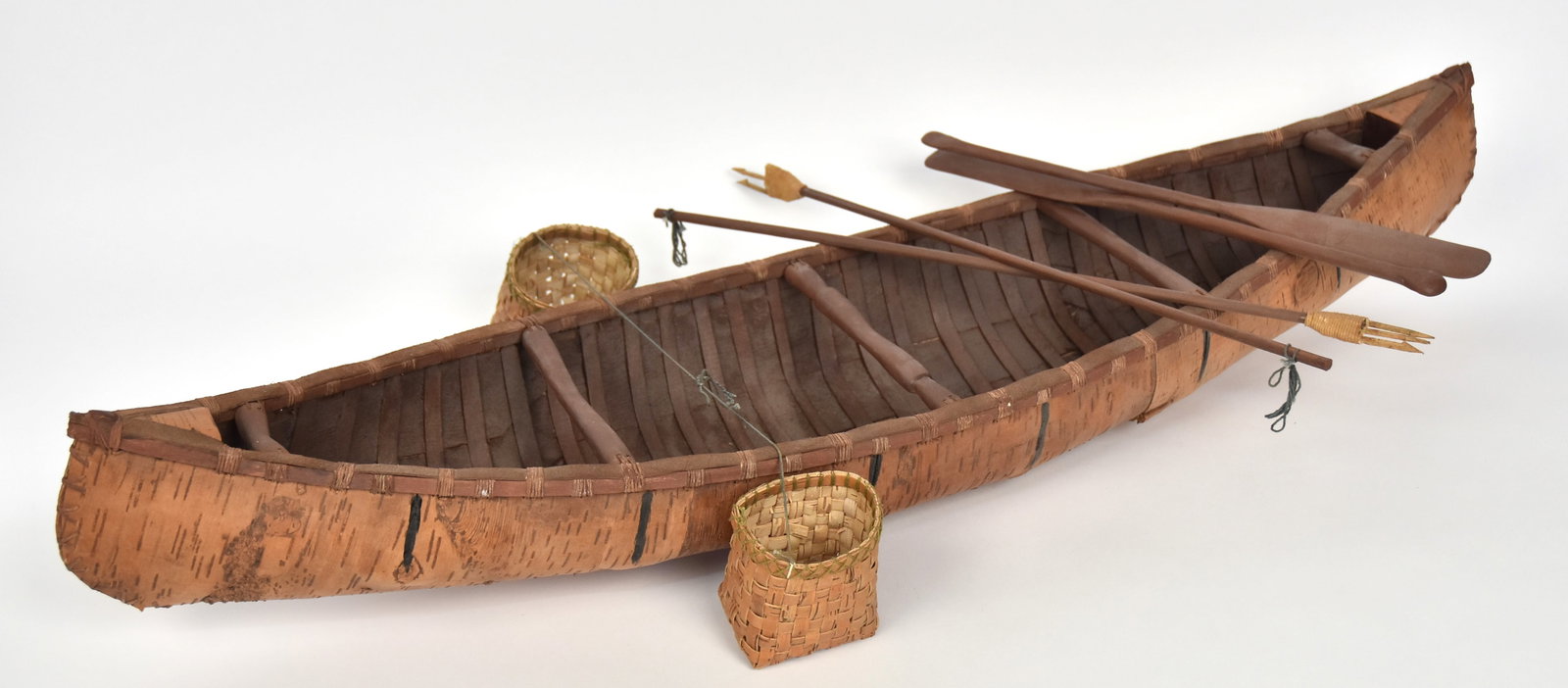 Fine Birch Bark Canoe Model: Circa first quarter of 20th century with two fish baskets, two wood paddles and two wood fish spears, 34 1/2" long x 8 3/4" wide x 7 3/4" high at prowl. Condition minor shrinkage, VG.