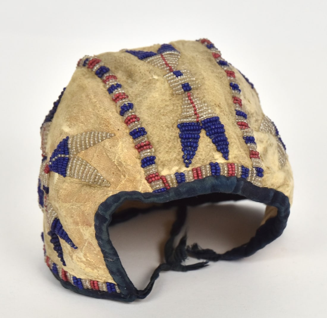 Sioux Infants Beaded Cap: Circa 1890-1900, on white buckskin with beaded geometric patter, blue velvet edging and white muslin liners
