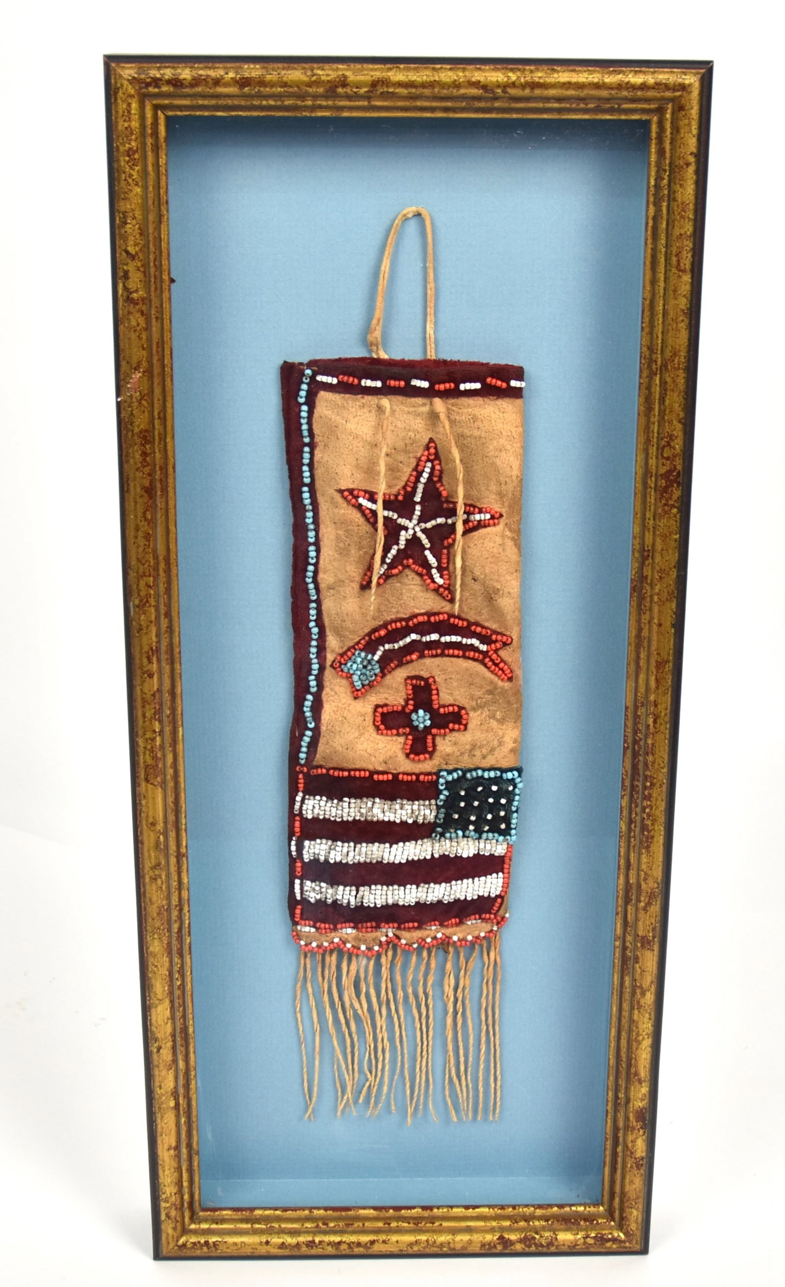 Patriotic Plains Beaded Pouch: Calf leather with red velvet edging decorated with U.S. flag at bottom with five-pointed stat, comet and cross above, belt loop and fringe, 3 x 8 1/2, less loop & fringe. Mounted in gilt shadowbox fra