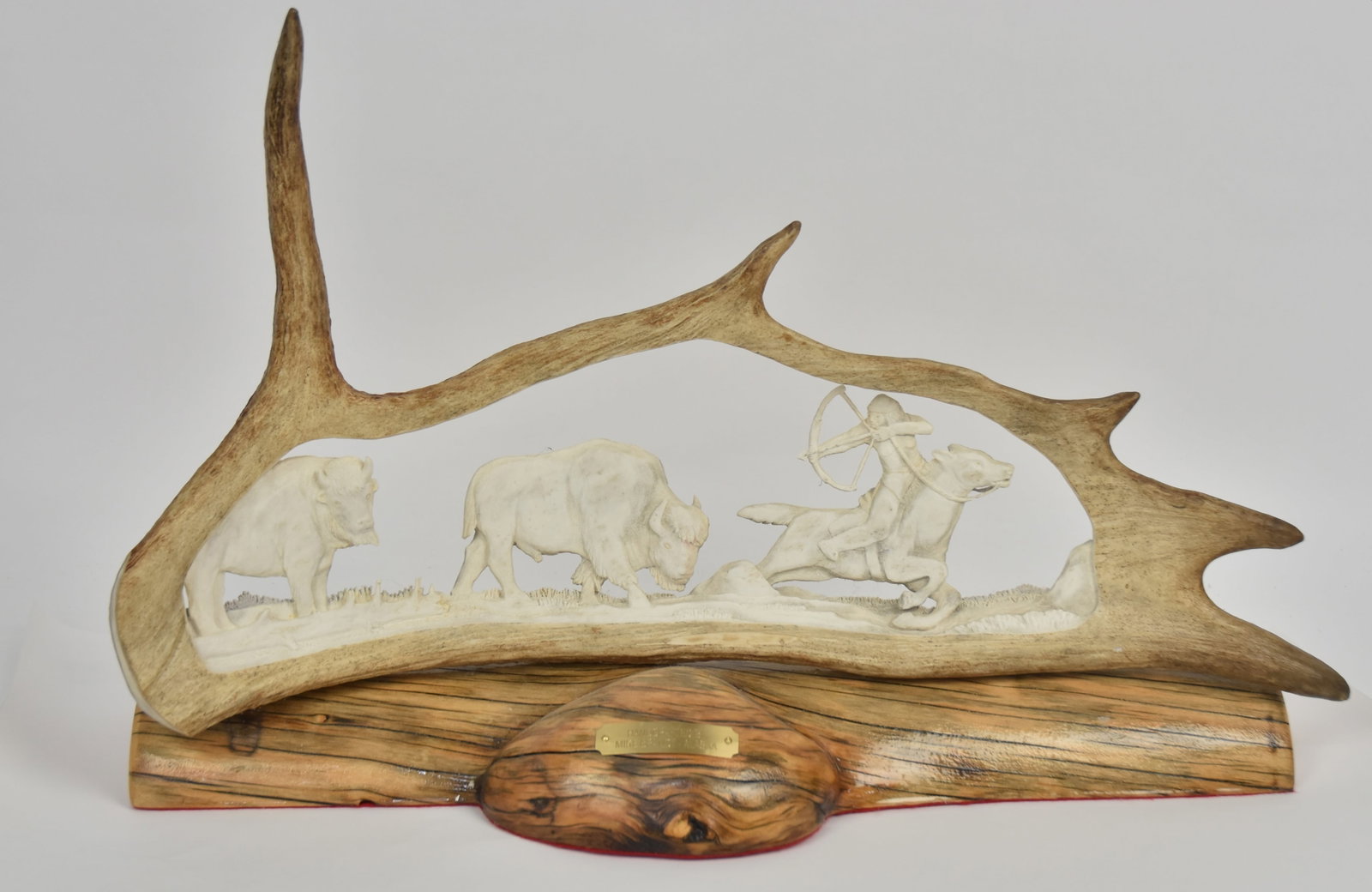 Mike Brandt Moose Antler Sculpture: Large section of antler, mounted on original drift wood base with brass tag reading: Handcrafted/Mike Brandt Alaska, carved with mounted Plains Native American hunting bison, 27 x8 x 17" high. Conditi