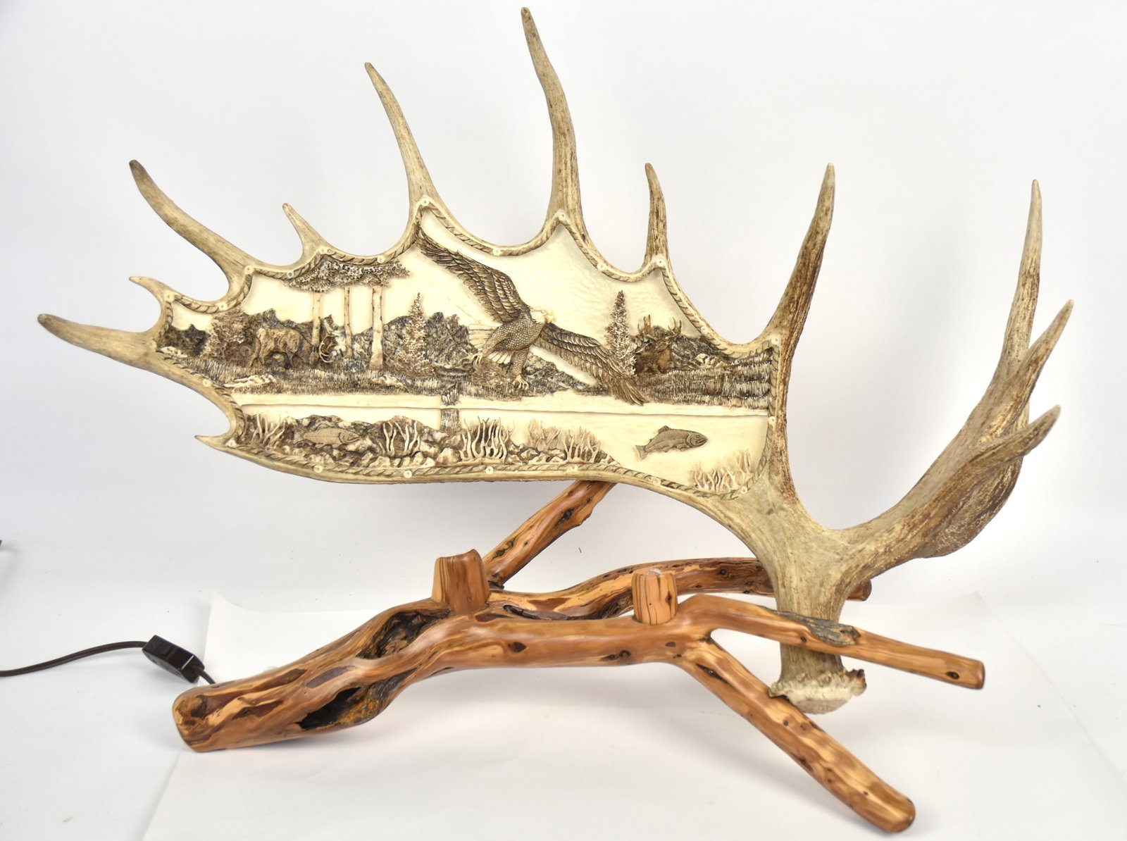 Dustin Nielson Moose Antler Sculpture: Deep relief carved full antler with Alaskan landscape with steam in which salmon are swimming while bald eagle is driving to catch one near surface, two elk in background, signed and dated on back Car