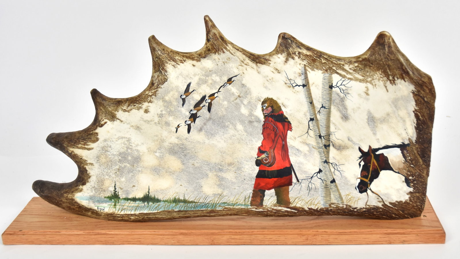 August Moose Antler Painting: Oil painting on the larger palm portion of moose antler showing an 18th century French trapper with his horse in march landscape with flock of Canada geese and birch trees, signed lower left, mounted 