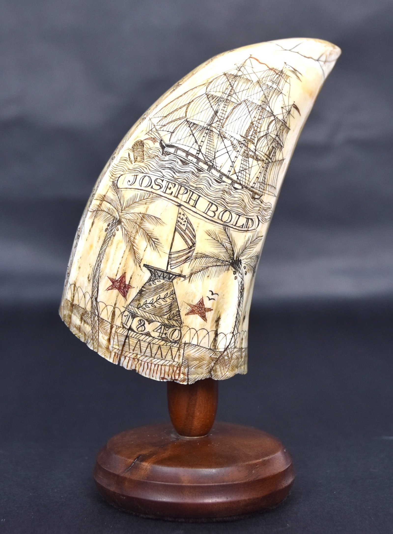 Fine Scrimshaw Sperm Whale Tooth: Engraved on each face with one having brig at full sail with breaching Sperm whale with ribbon banner inscribed Joseph Bold, over plinth with U.S. flag atop and 1840 flanked by two red 5-pointed stars