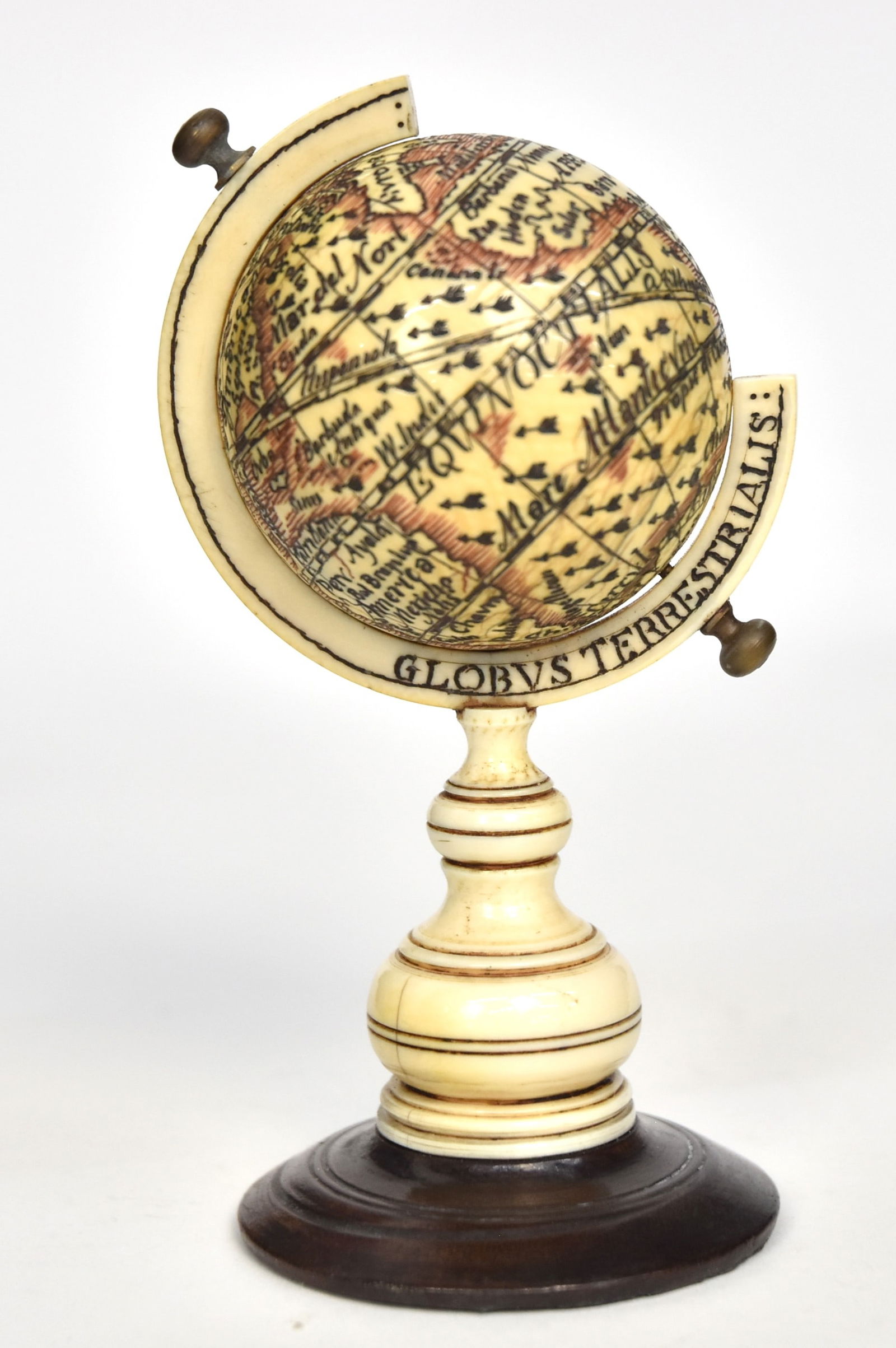 Scrimshaw Globe: Whale tooth ebony, brass & red and black pigments, turned spherical globe with engraved terrestrial landmasses with Latin script, mounted in on turned whale tooth 3/4 disc with engraved Latin Globus T