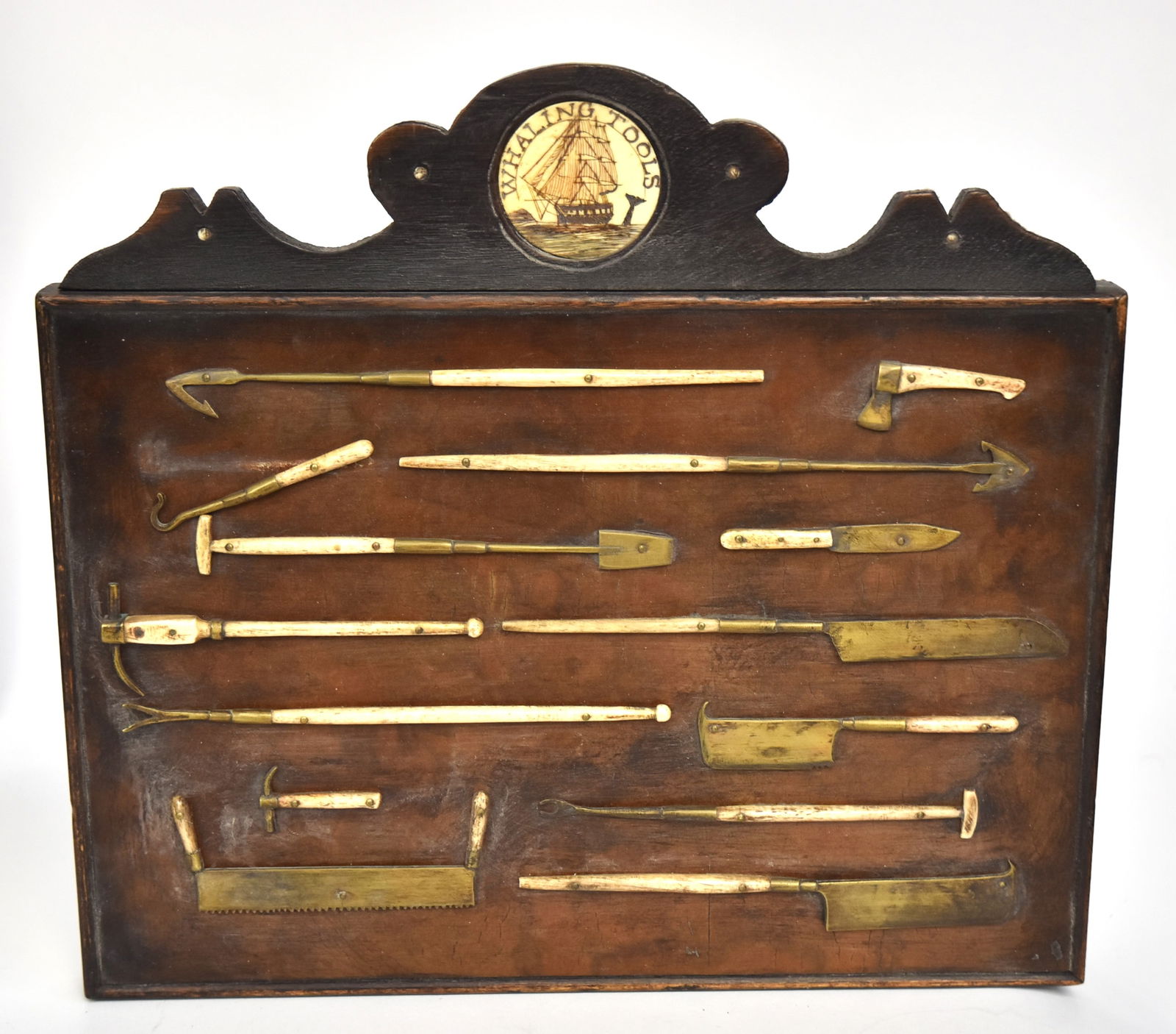 Miniature Scrimshaw Whaling Tools: Exotic hardwood plaque with scroll cut-out crest with inlaid whale tooth disc engraved with whaling ship, and diving whale with island in background and arched inscription above reading: Whaling Tools