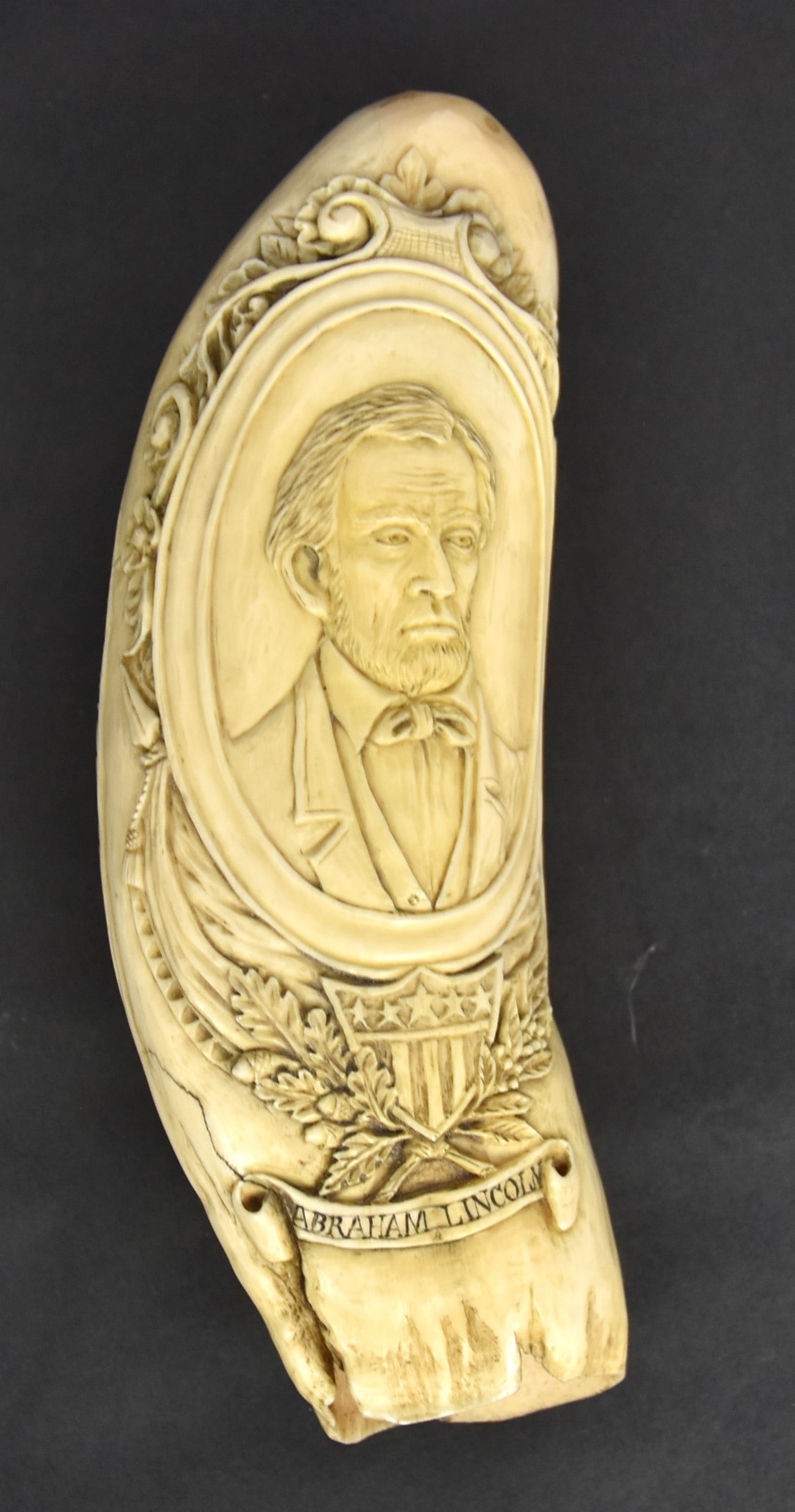 A. Lincoln Relief Carved Scrimshaw Sperm Whale Tooth: Beautifully carved on each face with shoulder length forward facing portrait of Lincoln in oval frame with floral scroll and drapery surround over U.S. shield with crossed oak & laurel branches, above