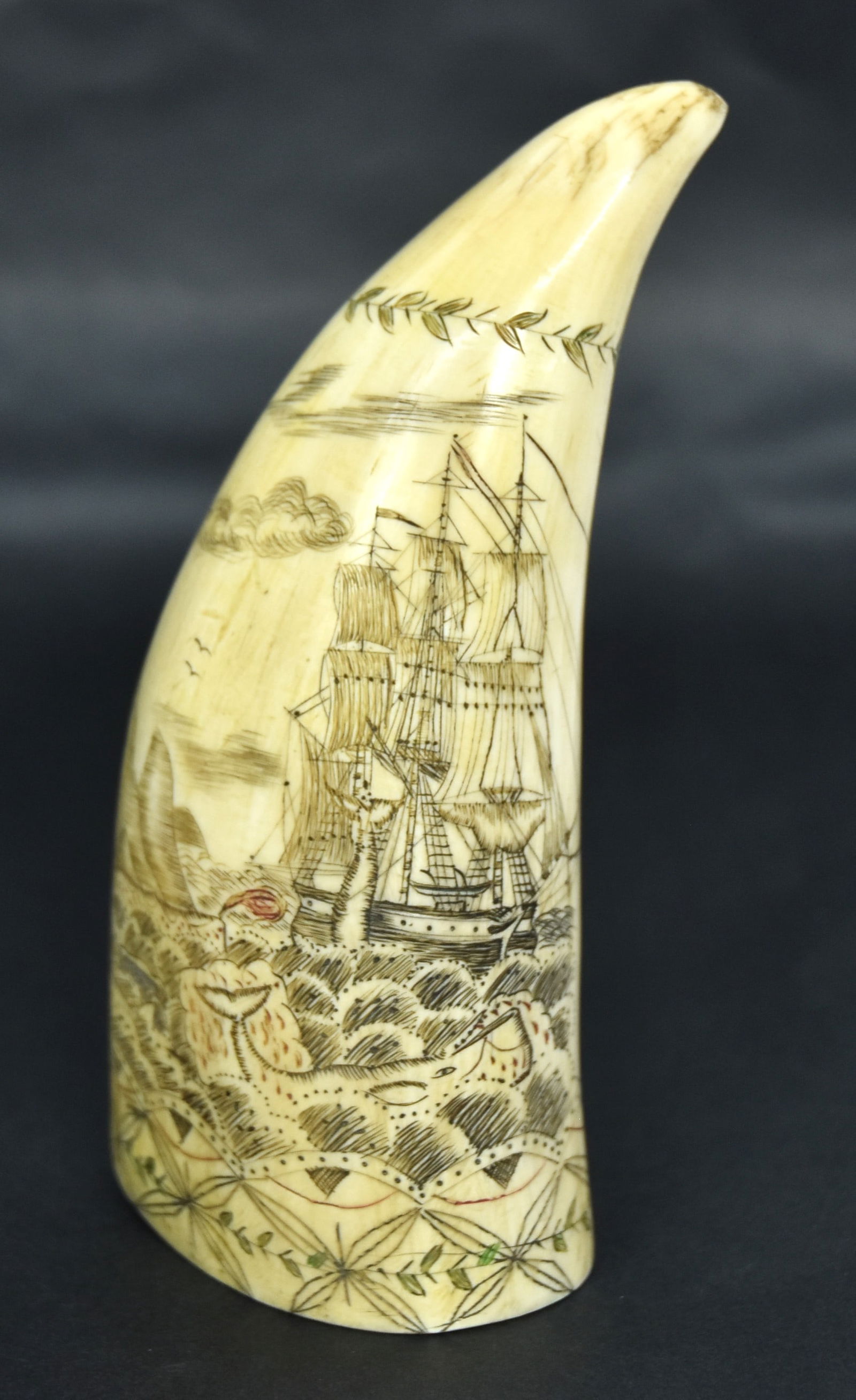Fine Scrimshaw Sperm Whale Tooth: Engraved on each face with obverse having whaler lifting a whale to be dismembered, while 2 other whales are to left and foreground, island or ergs to left; reverse with sailor atop whale holding harp