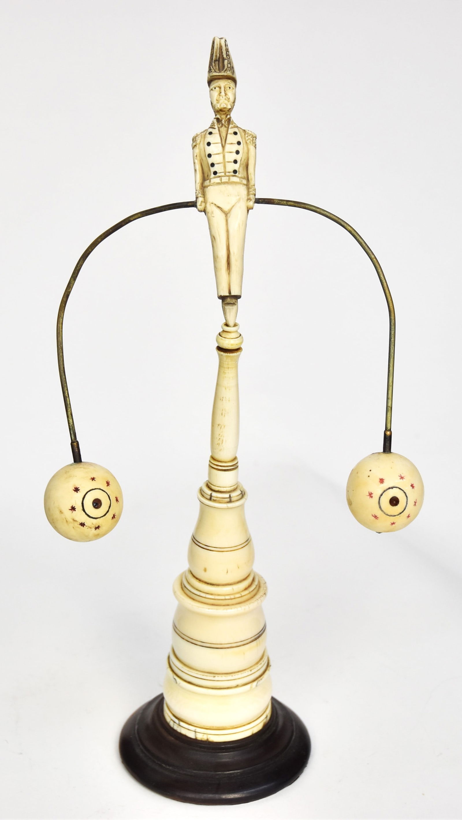 Fine Scrimshaw Figural Toy: Whale tooth, baleen, brass and ebony, figure of a naval officer with inlaid baleen buttons holding brass bent pole with whale tooth balls at terminals, mounted on turned whale tooth column with turned