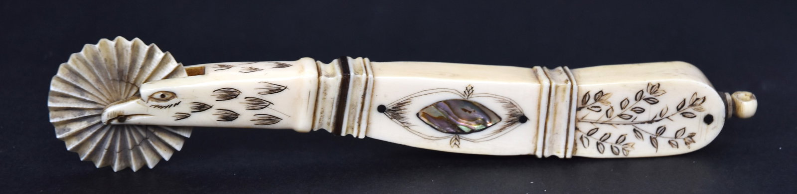 Fine Figural Scrimshaw Jagging Wheel: Whales tooth, baleen and abalone with single fluted crimping whee with eagles head mount with engraved and carved details, grip with baleen band, dots and horn band, engraved floral and inlaid abalone