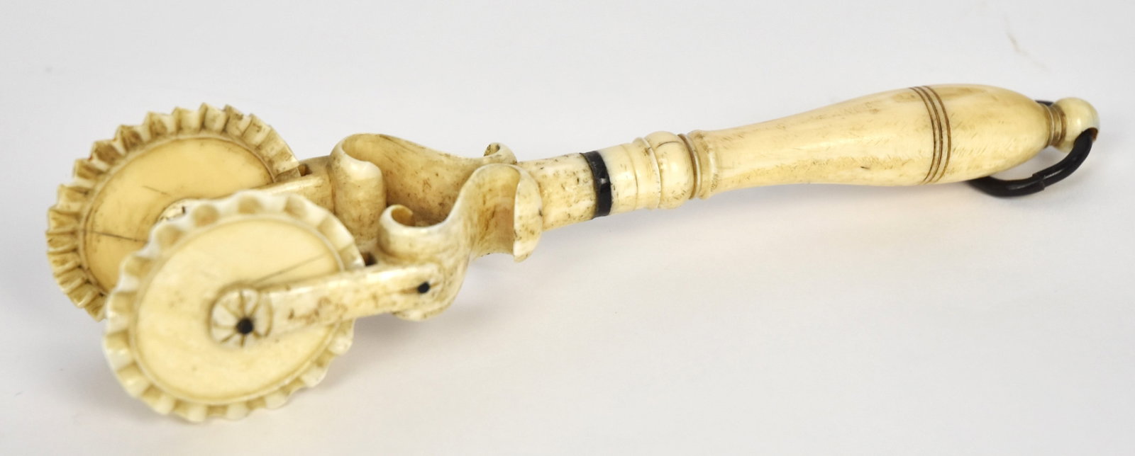 Fine Scrimshaw Jagging Wheel: Pie Crimper, in walrus and baleen, with double fluting wheels, mounted on S scrolls with turned grip with one baleen ring and baleen ring at terminal for hanging, nice patina, 7 3/4" long. Condition F