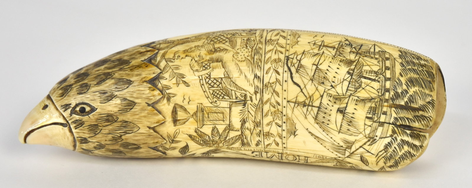 Fine Scrimshaw Sperm Whale Tooth: Engraved on each face with obverse having lovely basket of fruit and flowers with Home Sweet Home below and tip engraved as eagle head; reverse with three masted ship at bottom with band of laurel bra