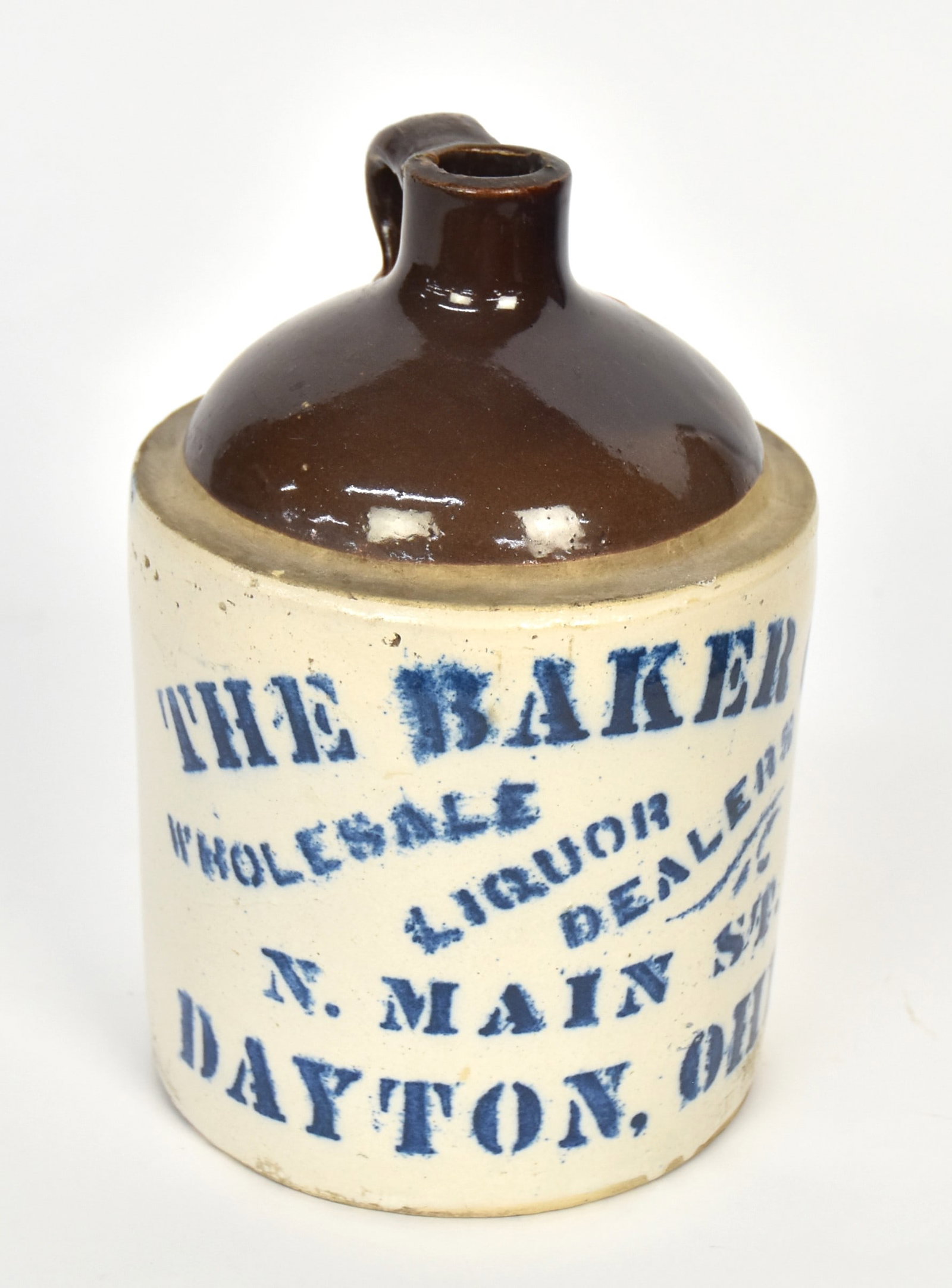 The Baker Co. Dayton, Ohio Stoneware Jug: Two toned brown and white stoneware with stenciled cobalt:The Baker Co./Wholesale Liquor Dealers/N. Main St./Dayton, Ohio., 5 1/2" diameter x 8 3/4" high. Condition Fine.
