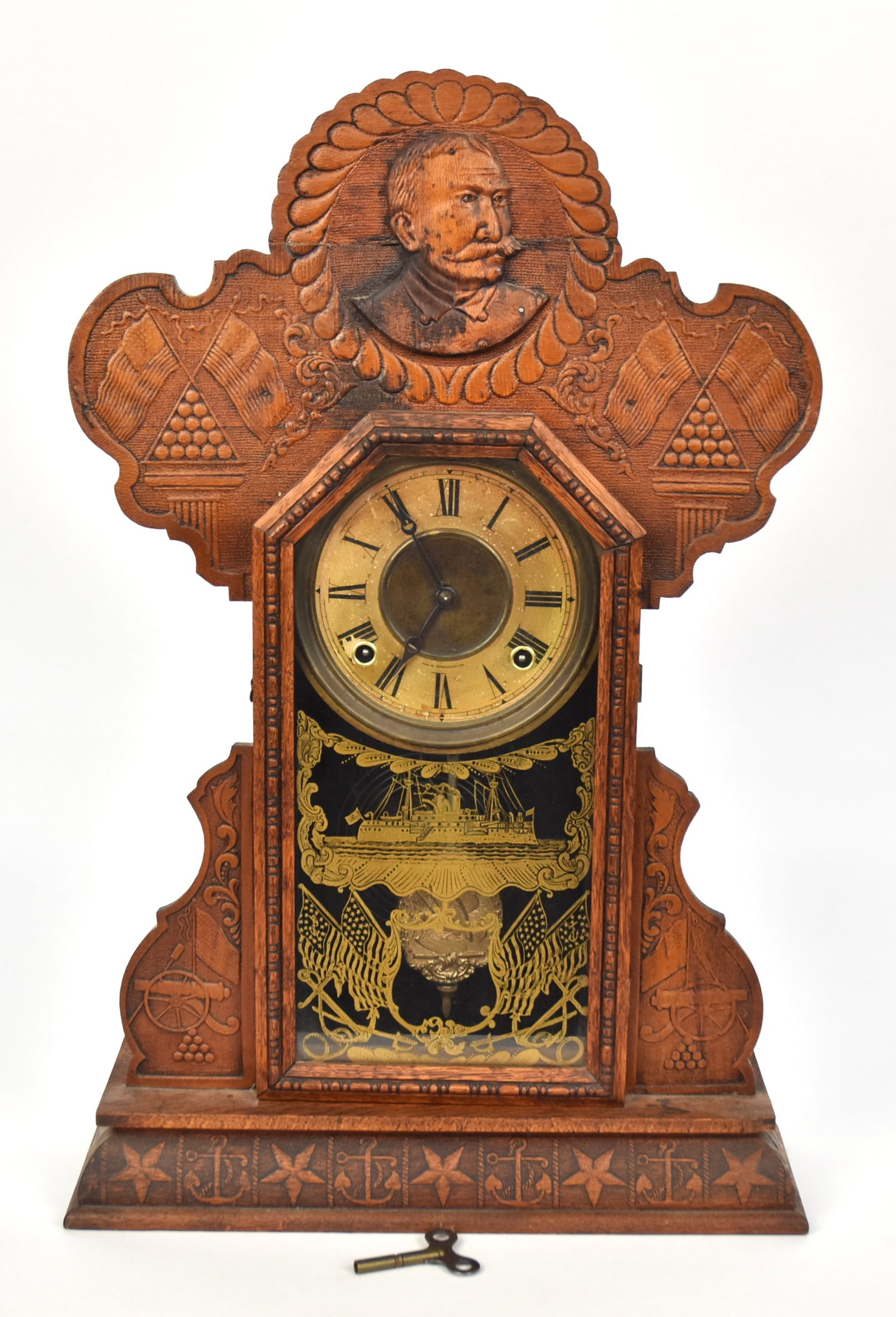 Admiral Dewey Ingraham Oak Shelf Clock: Circa 1899 with pressed case with shoulder length portrait in crest, flanked by military motifs, printed dial marked The E. Ingraham Co., gilt glass door with battleship and crossed flags, eight day s
