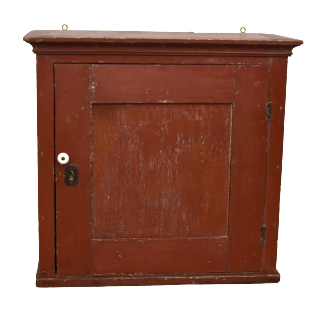 Red Painted Dovetailed Hanging Cupboard: Mixed woods, cove molded top over single paneled door with original porcelain knob and cast iron escutcheon solid ends and base with stepped stripe, in original red painted finish, interior with four 