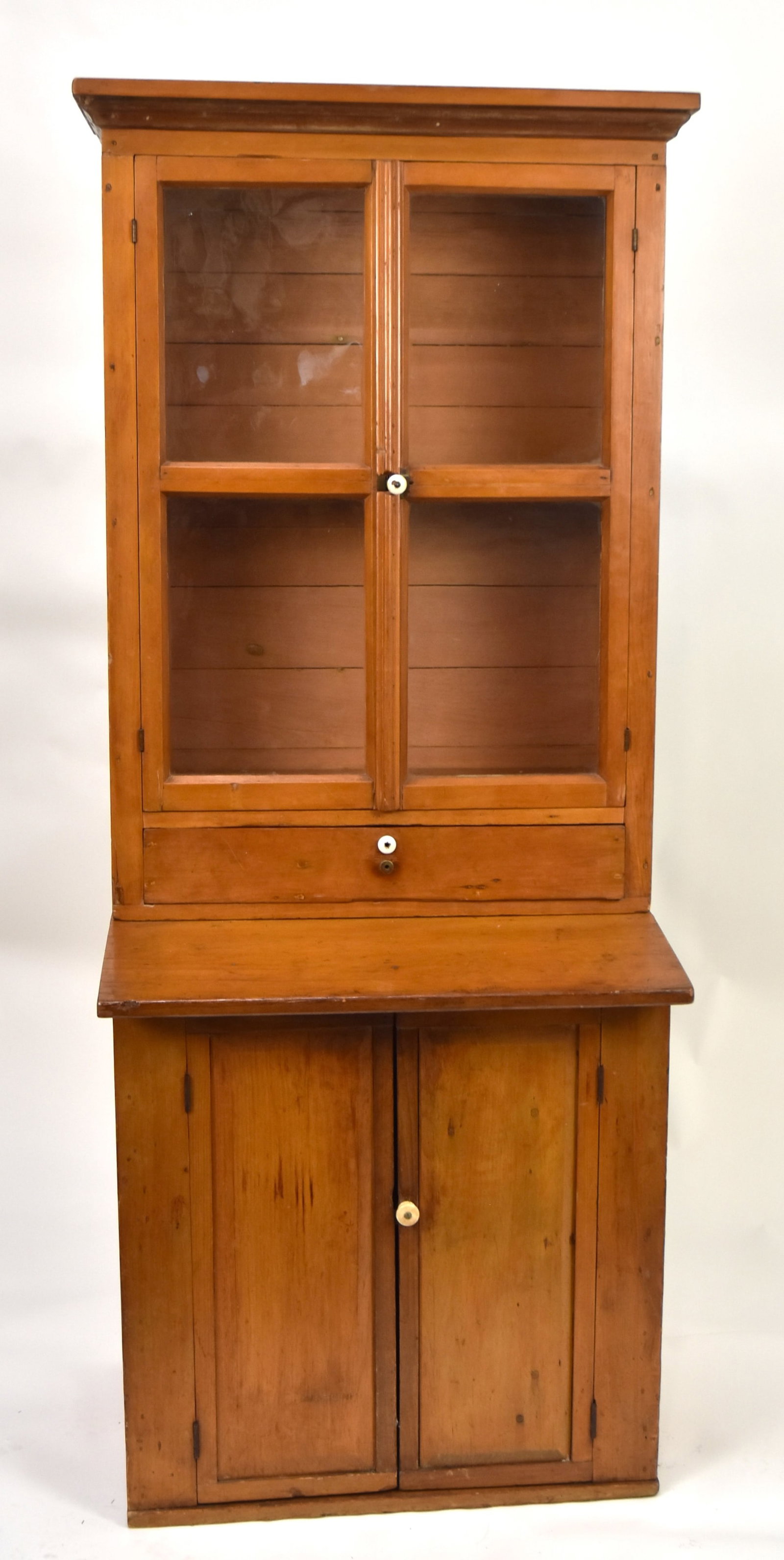 Small Primitive Step-Back Cupboard: White Pine in two pieces with cove molded top, over two glass doors, each with two lights, over single drawer, over slant work surface, over two paneled doors, base with paneled sides, interior each w