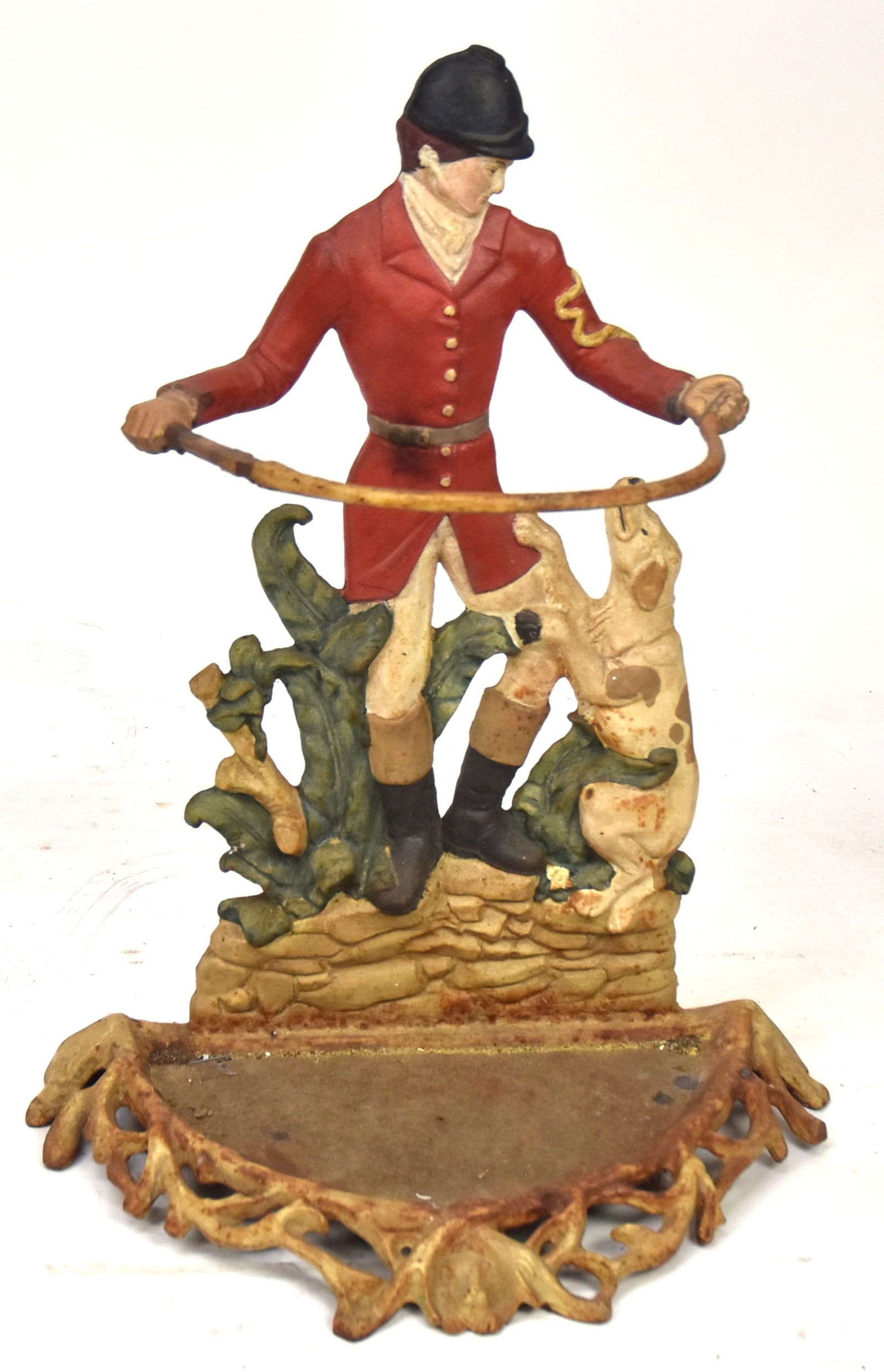 Cast Iron Figural Umbrella Stand: Polychrome painted figure of a gentleman in hunting clothing holding a bent whip in both hands, thus forming the bar to hold the umbrellas in with leaping hound and floral, standing on rock out-crop,