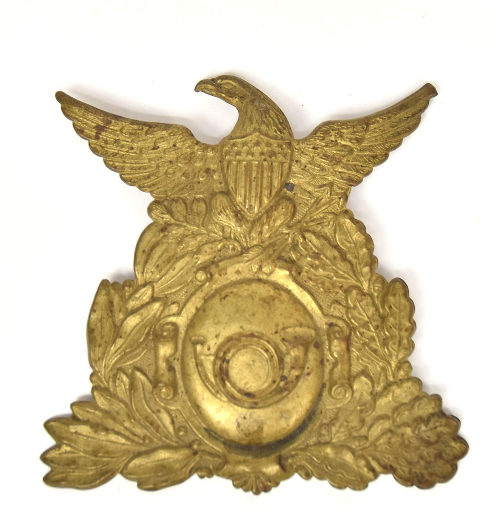 American Brass Cap Badge: Circa 1810-30 stamped brass with U.S. shield breasted spread wing eagle clutching arrows and laurel branch in talons, over oval crest with trumpet, and laurel and oak leaf wreath surround, 4" wide x 4