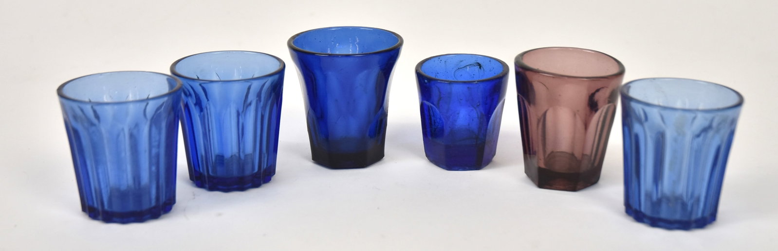 Six Colored Flint Glass Flips: Shot size, five in cobalt, three of them vertical ribbed, one in purple, from 1 7/9" to 2 1/4" diameter x 2" to 2 1/2" high. Condition All VG.