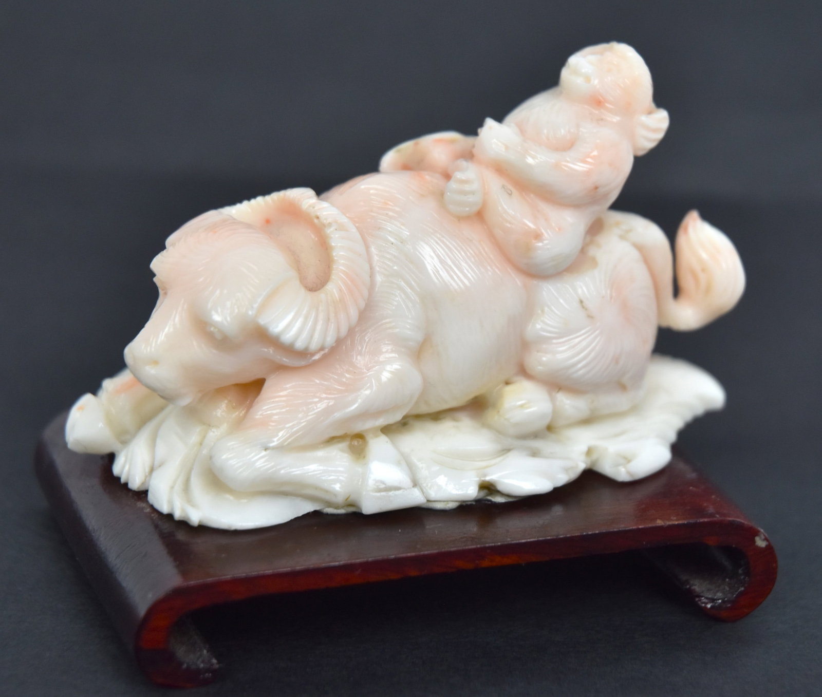 Chinese Carved Coral Water Buffalo & Monkey: White coral with pink tint monkey riding a water buffalo, mounted on teak stand, 3 x 1 1/4 x 2 1/2" high. Condition Fine.